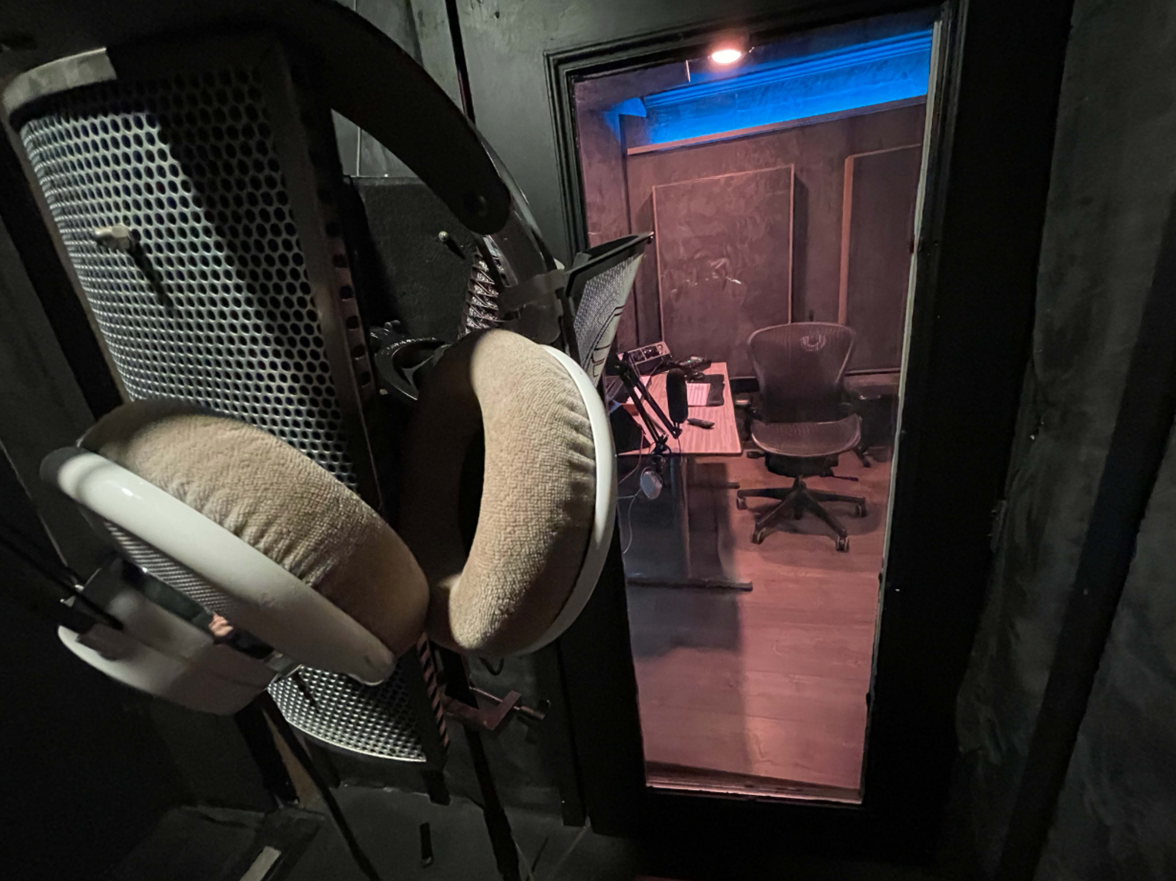 A recording studio is visible through a glass door, featuring a desk with equipment and a chair.