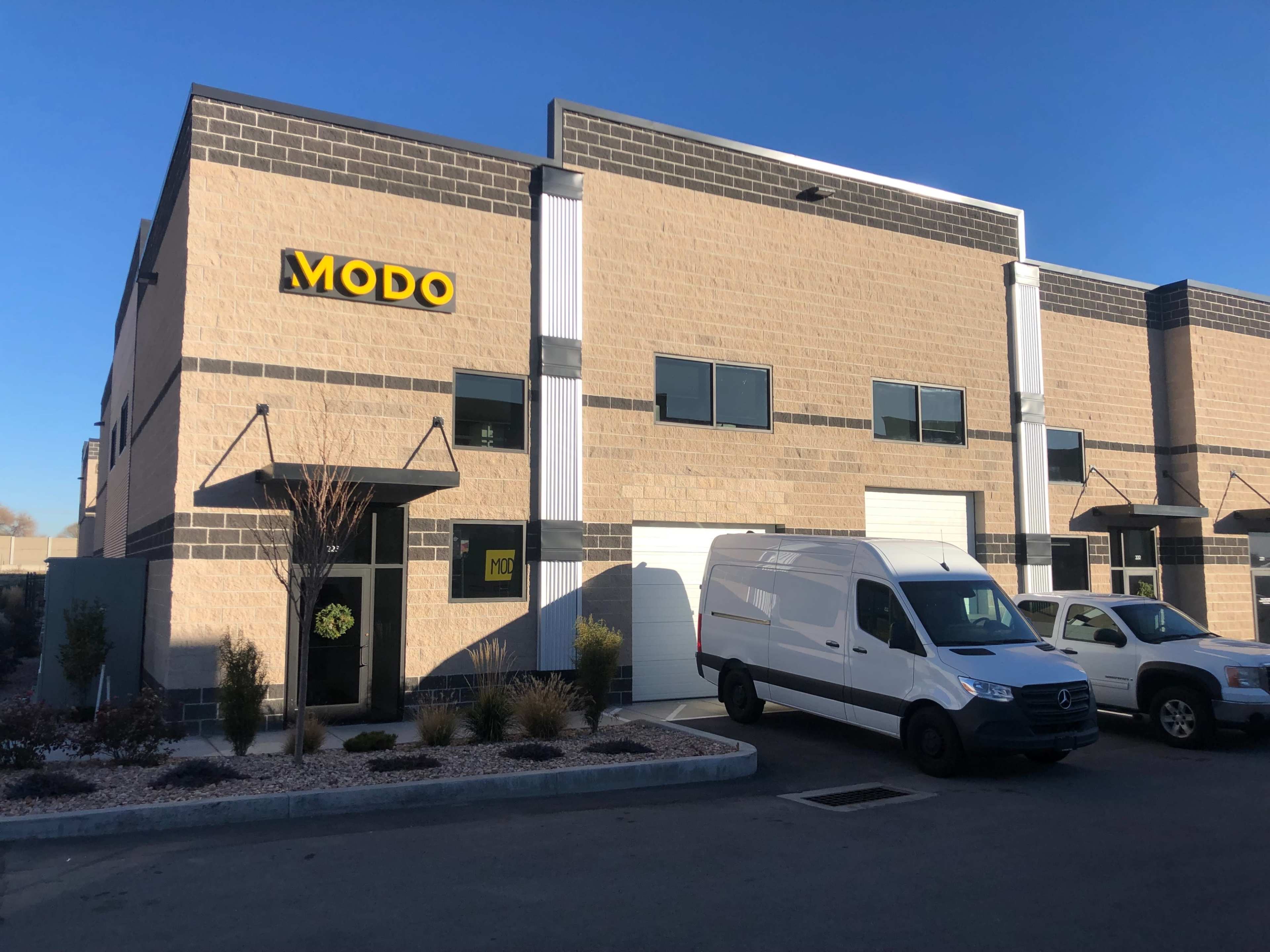 A commercial building with a prominent "MODO" sign, featuring two parked vehicles in front.