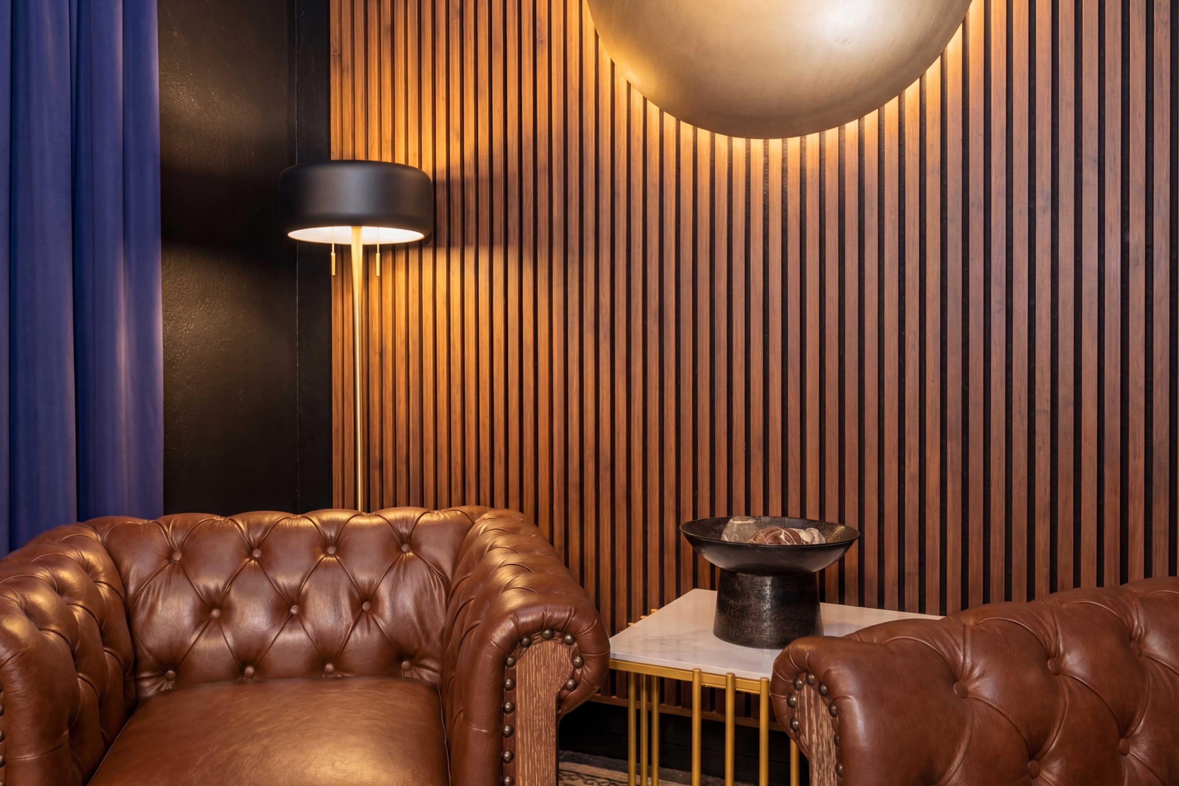 A cozy seating area features two leather chesterfield chairs, a marble-topped table, and a lamp against a wooden-paneled wall.