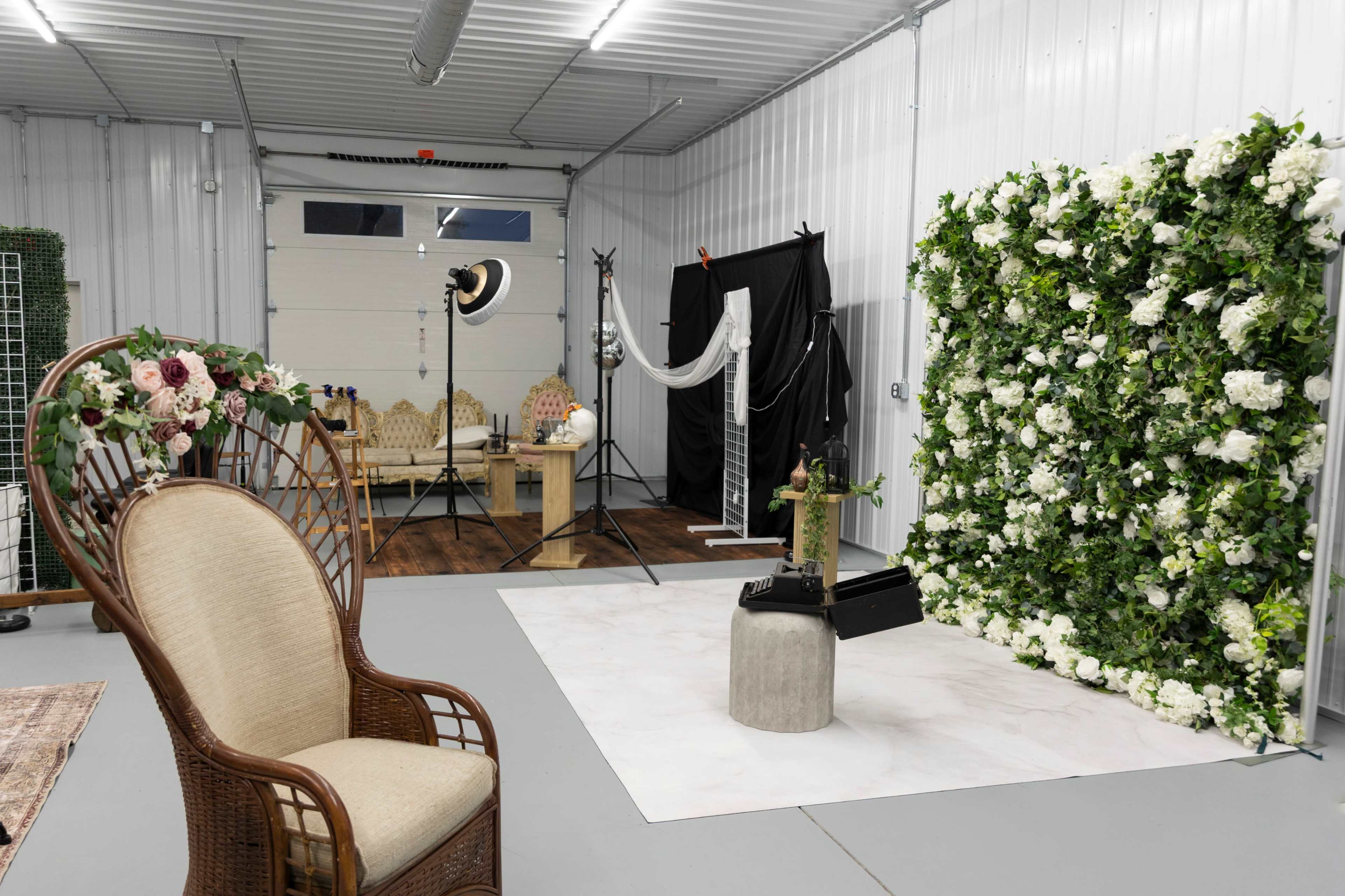 The image shows a photography studio featuring a floral backdrop, a chair, and various photography equipment arranged in a well-lit space.