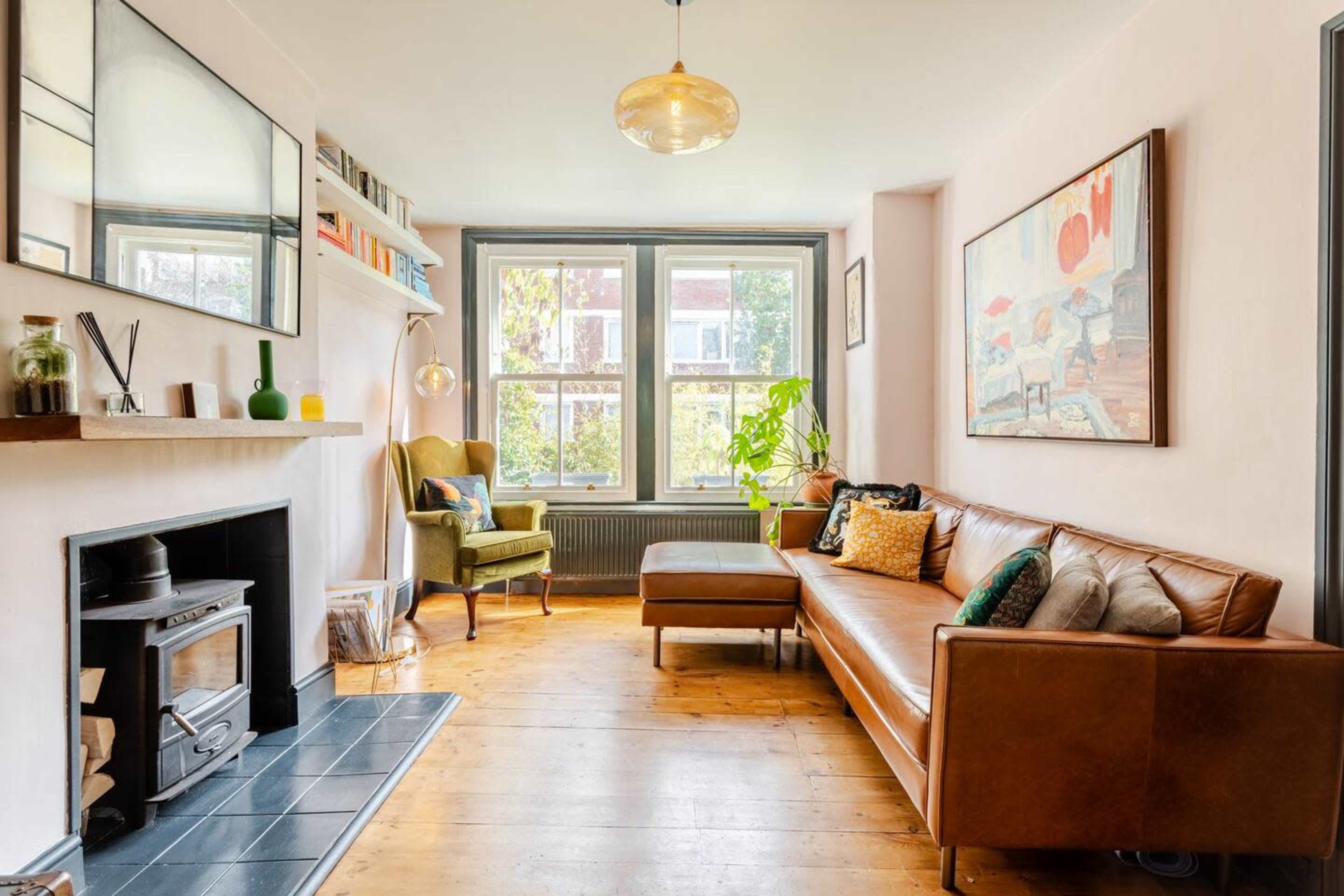 The living room features a brown leather sofa, a fireplace, a plant near the window, and artwork on the walls.