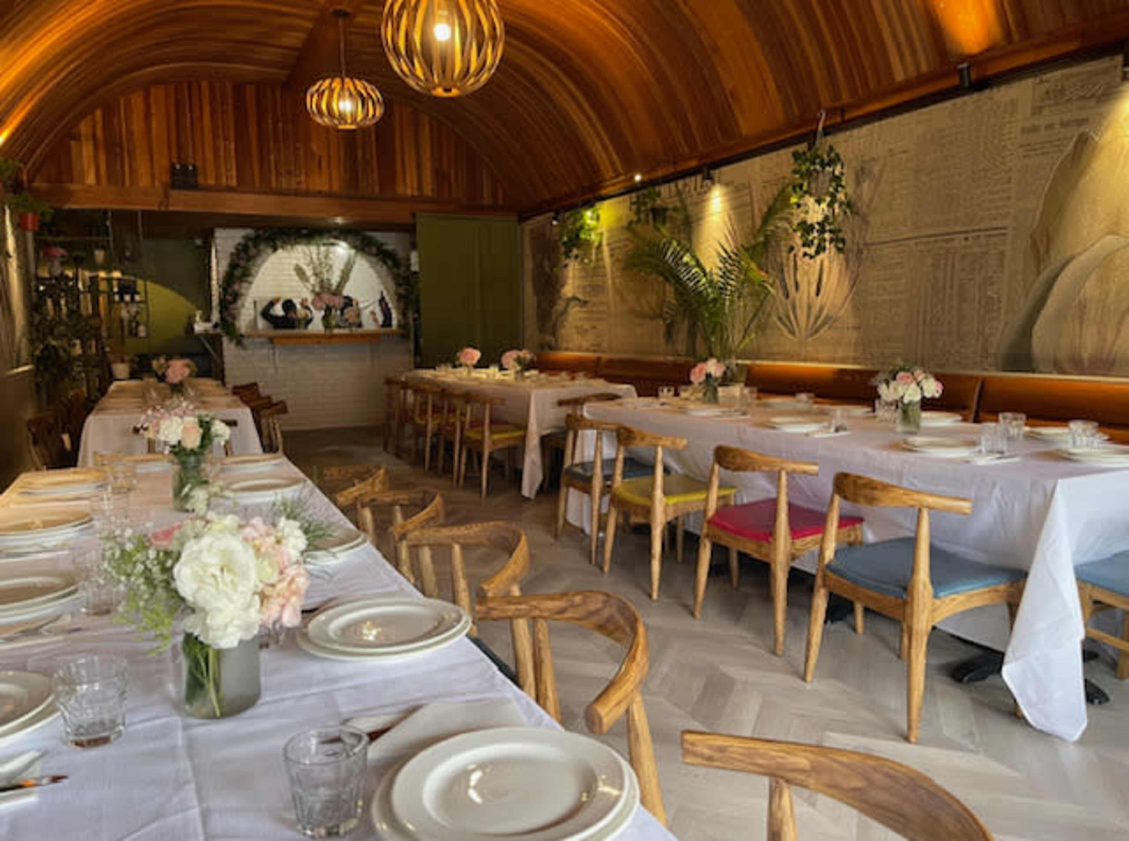 A restaurant interior with wooden paneling, long tables set for dining, and floral centerpieces.