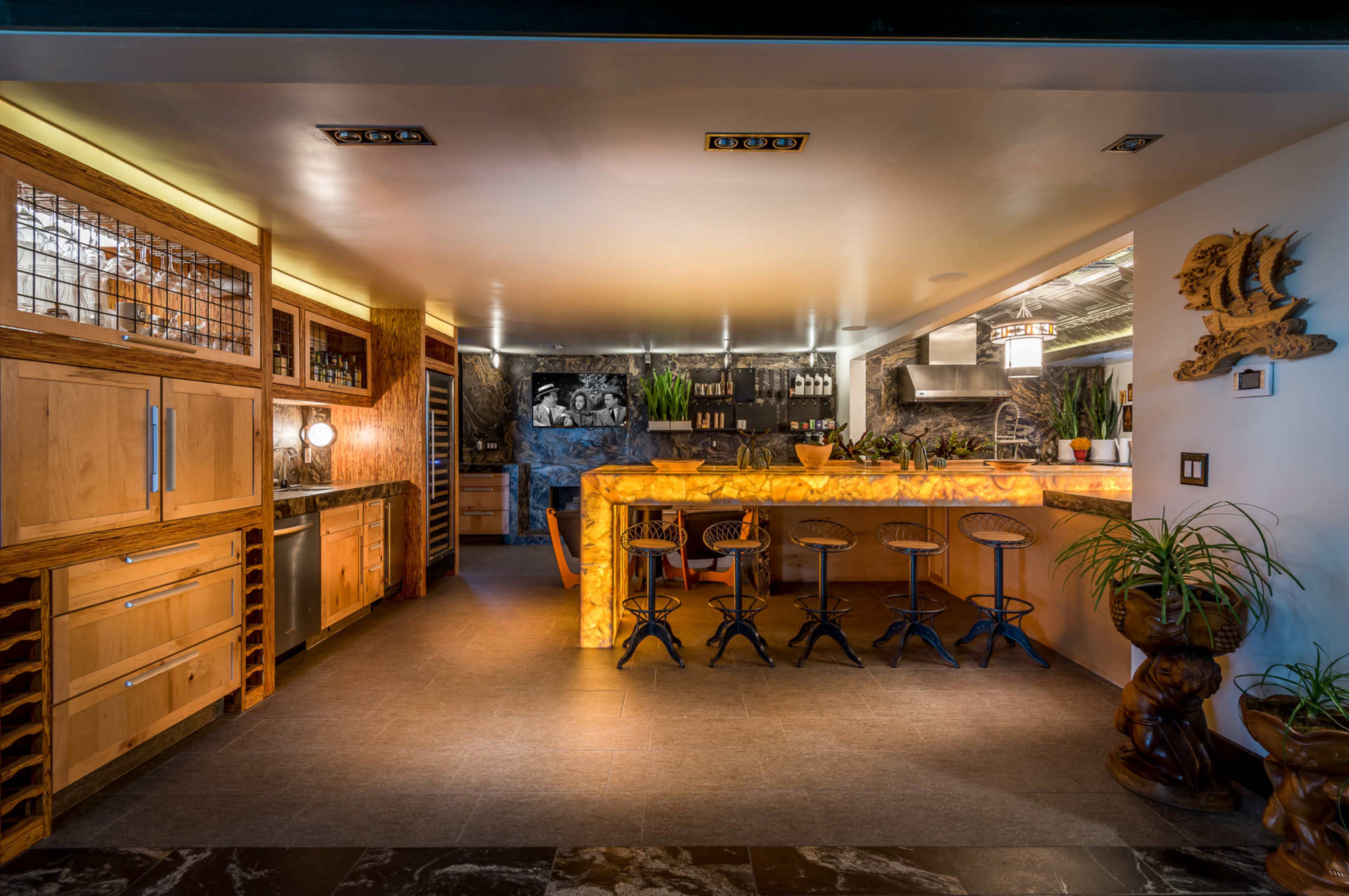 A modern kitchen and bar area with wooden cabinetry, a large, curved bar counter, and a seating arrangement with high stools.
