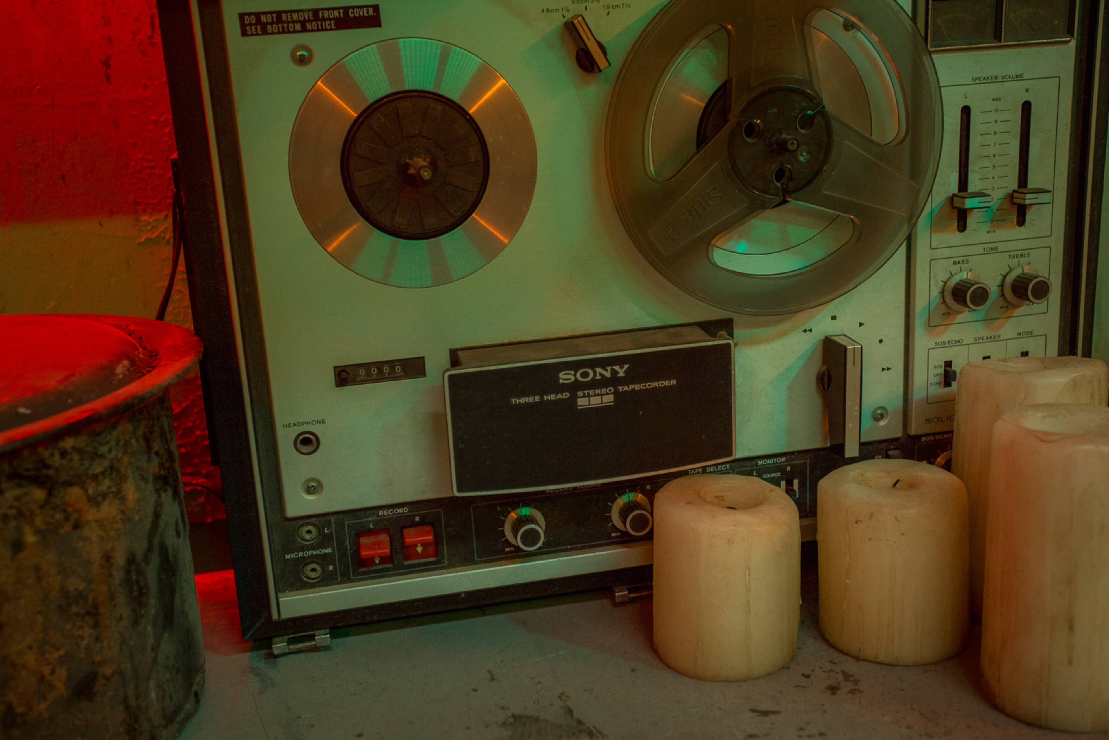 A vintage Sony reel-to-reel tape recorder positioned alongside two white candles on a textured surface.