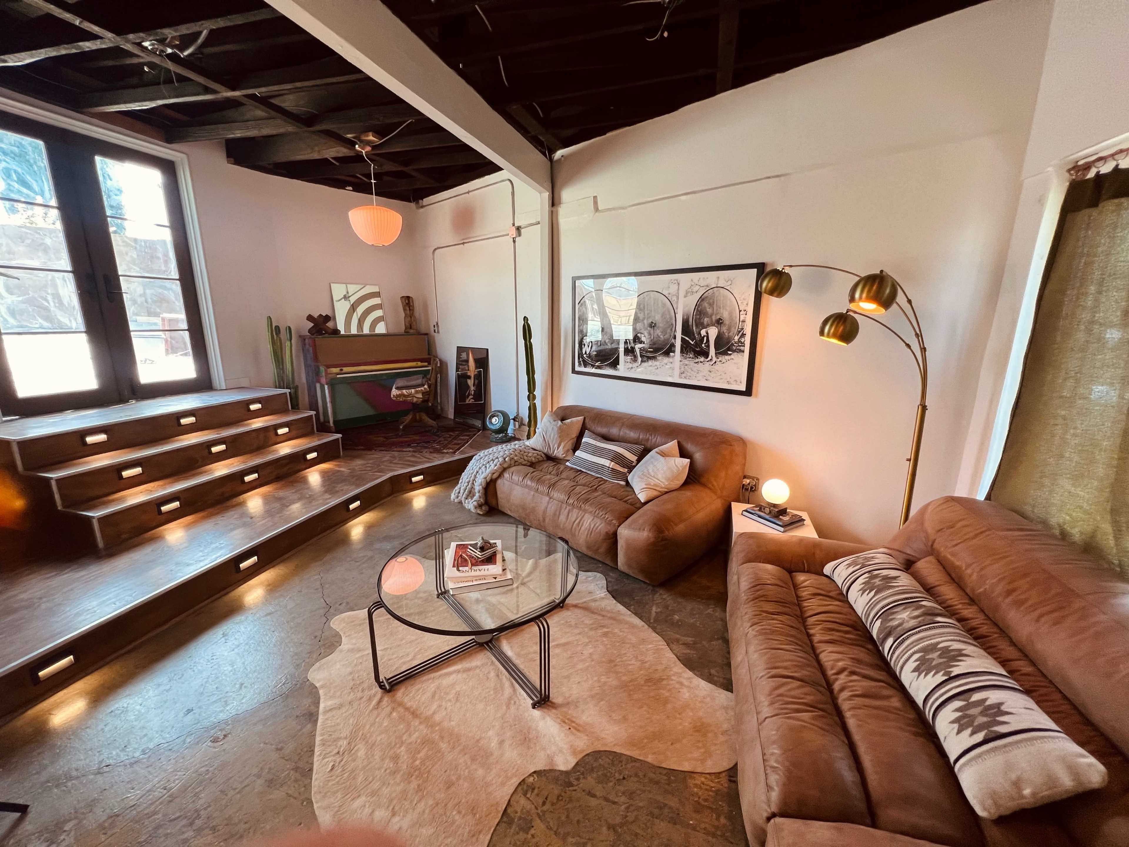 The room features a sunken seating area with two brown sofas and a circular glass coffee table, illuminated by various light sources and surrounded by decorative elements.