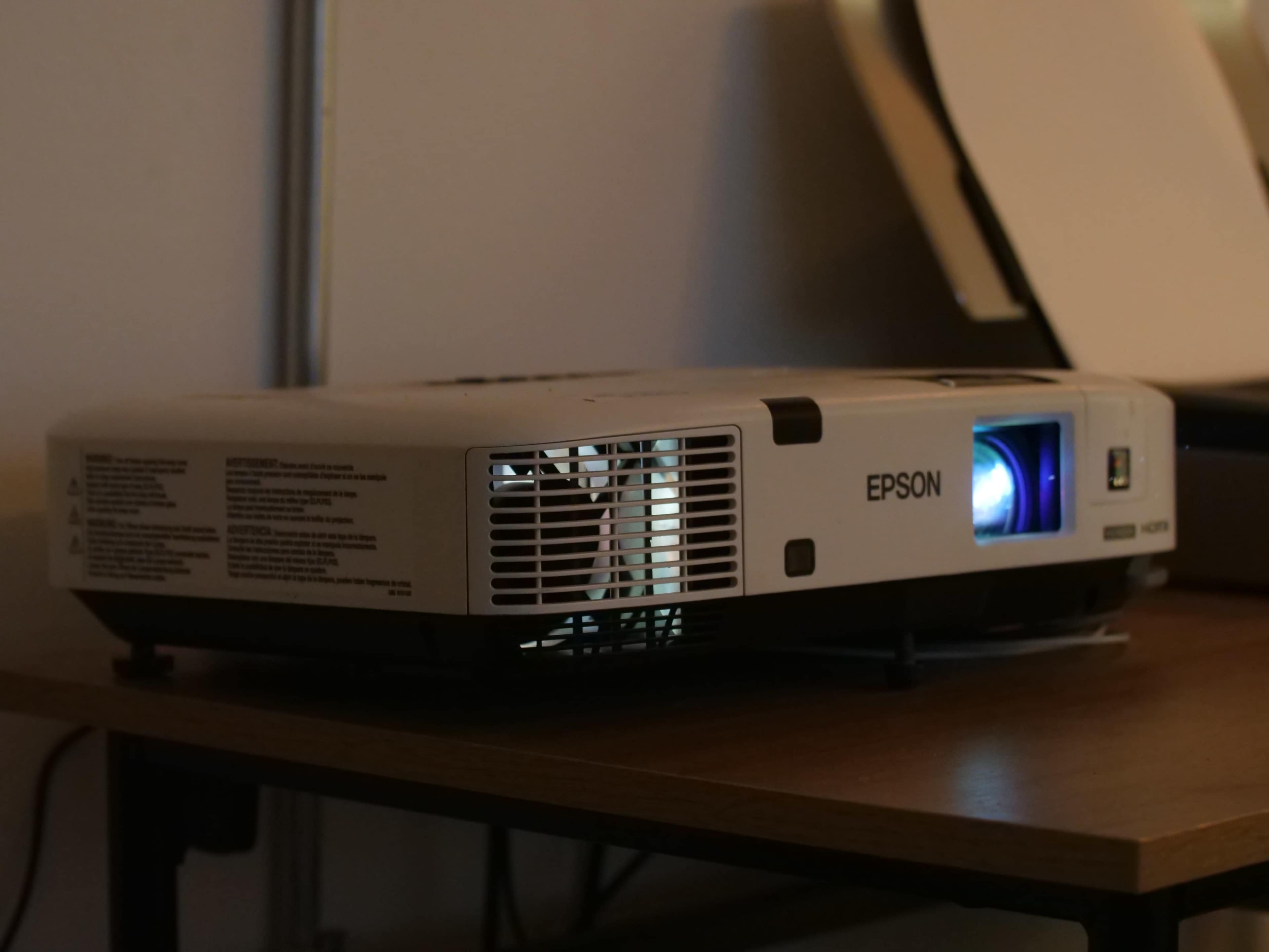 An Epson projector sits on a wooden table, emitting light from its lens.