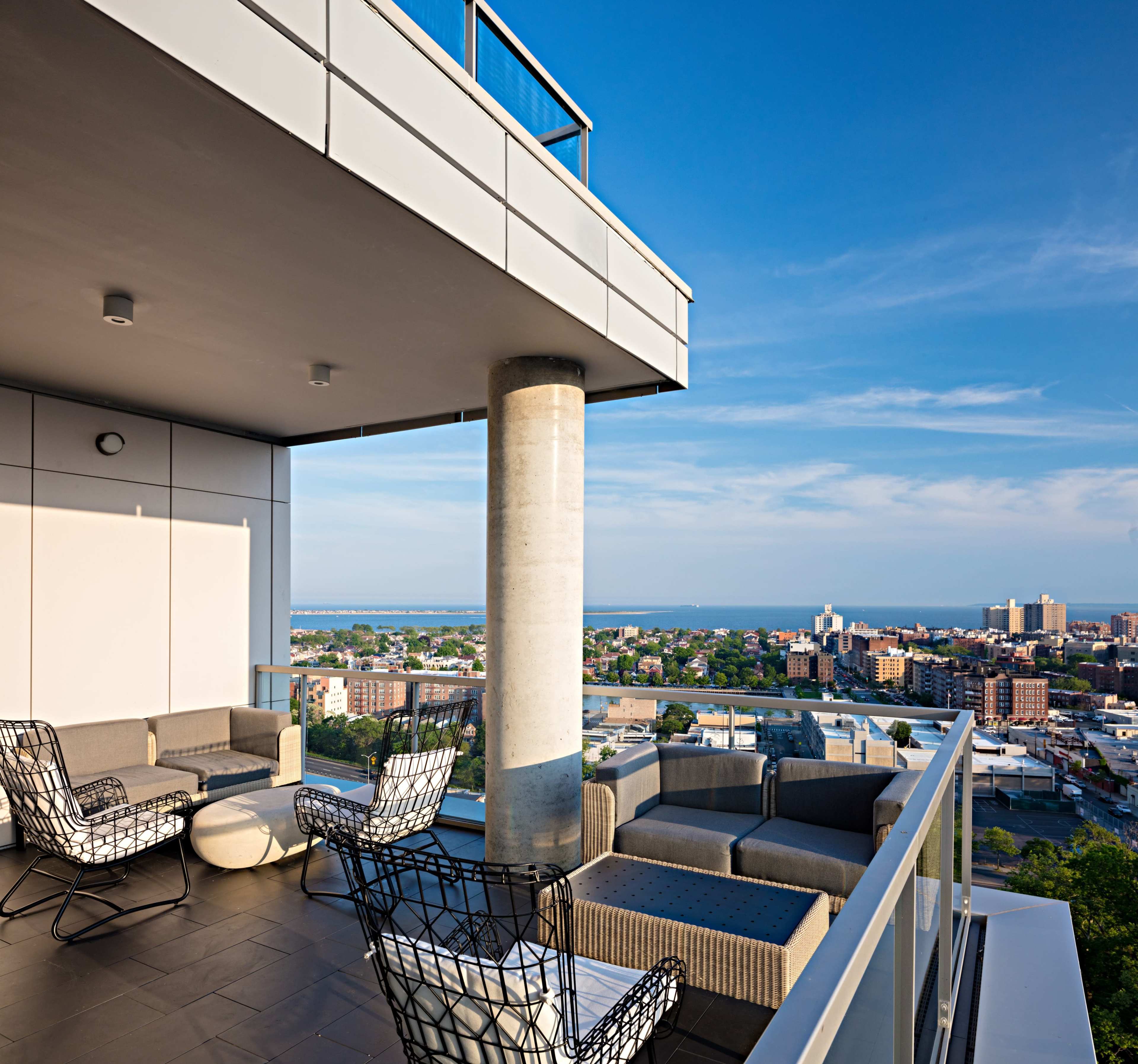 A rooftop terrace with modern seating overlooks a cityscape and water in the distance.