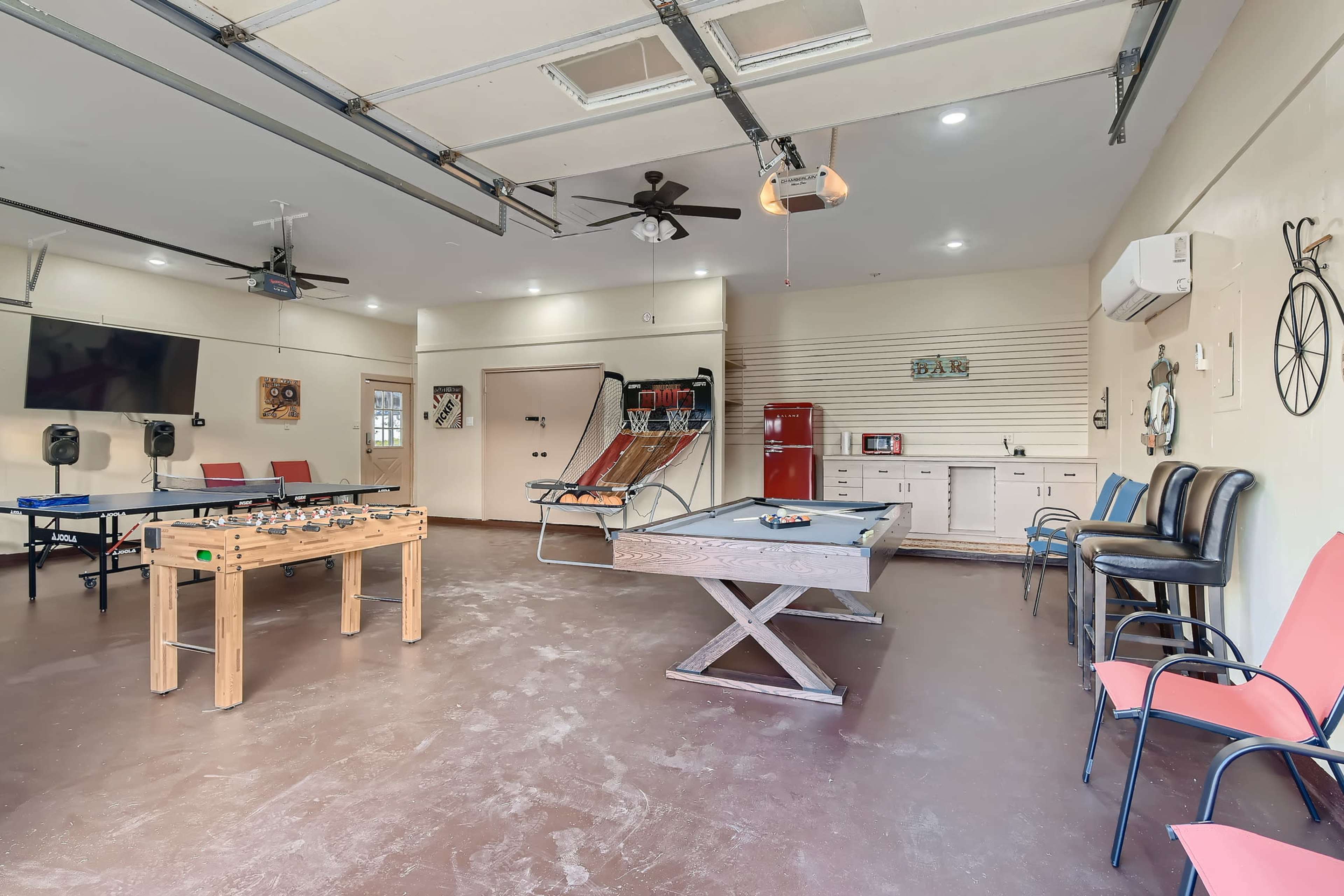 The image shows a recreational room featuring a foosball table, a pool table, and various seating arrangements, along with a retro refrigerator and entertainment equipment.