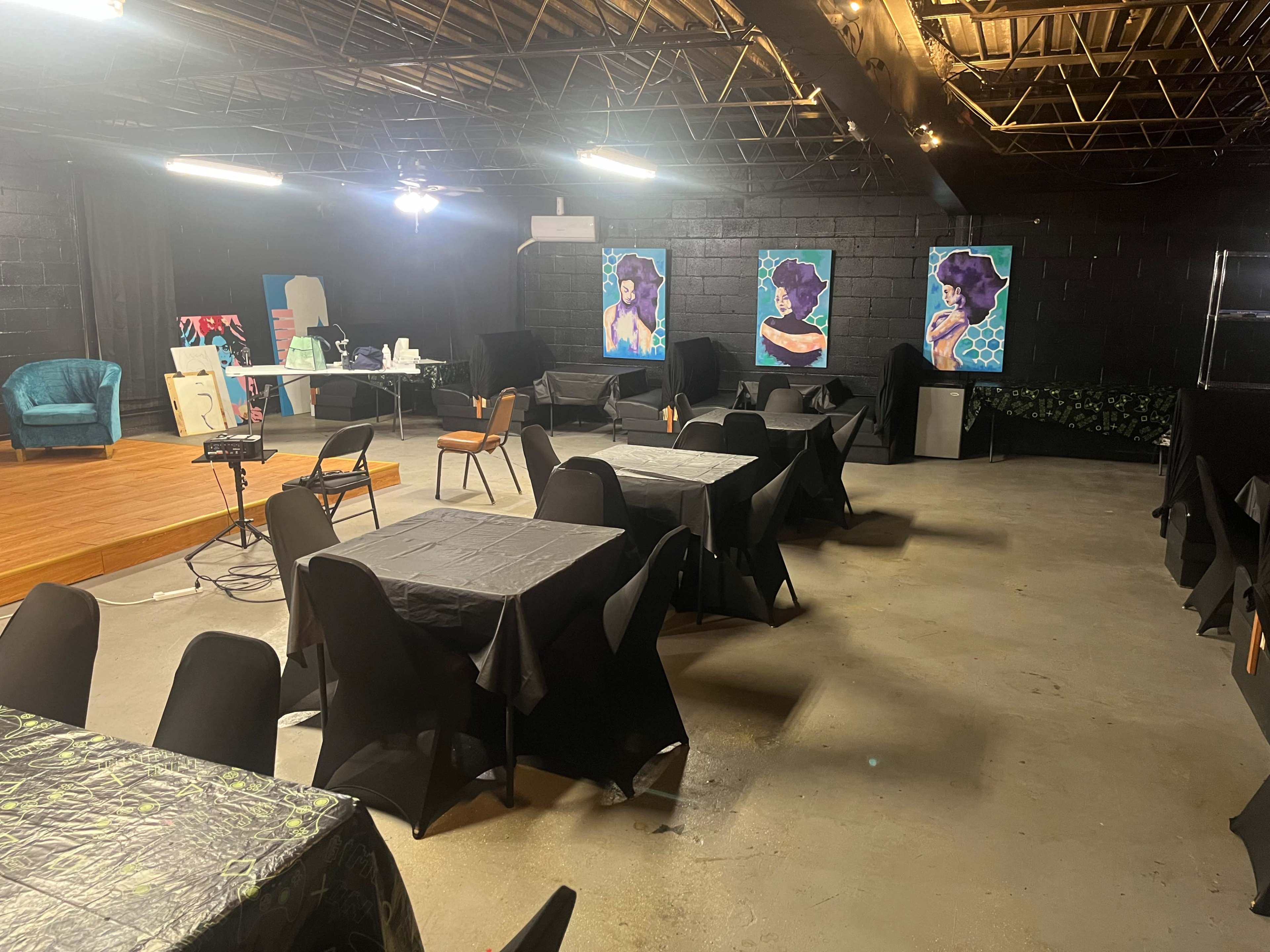An empty event space with black-covered tables and two colorful paintings on the walls.