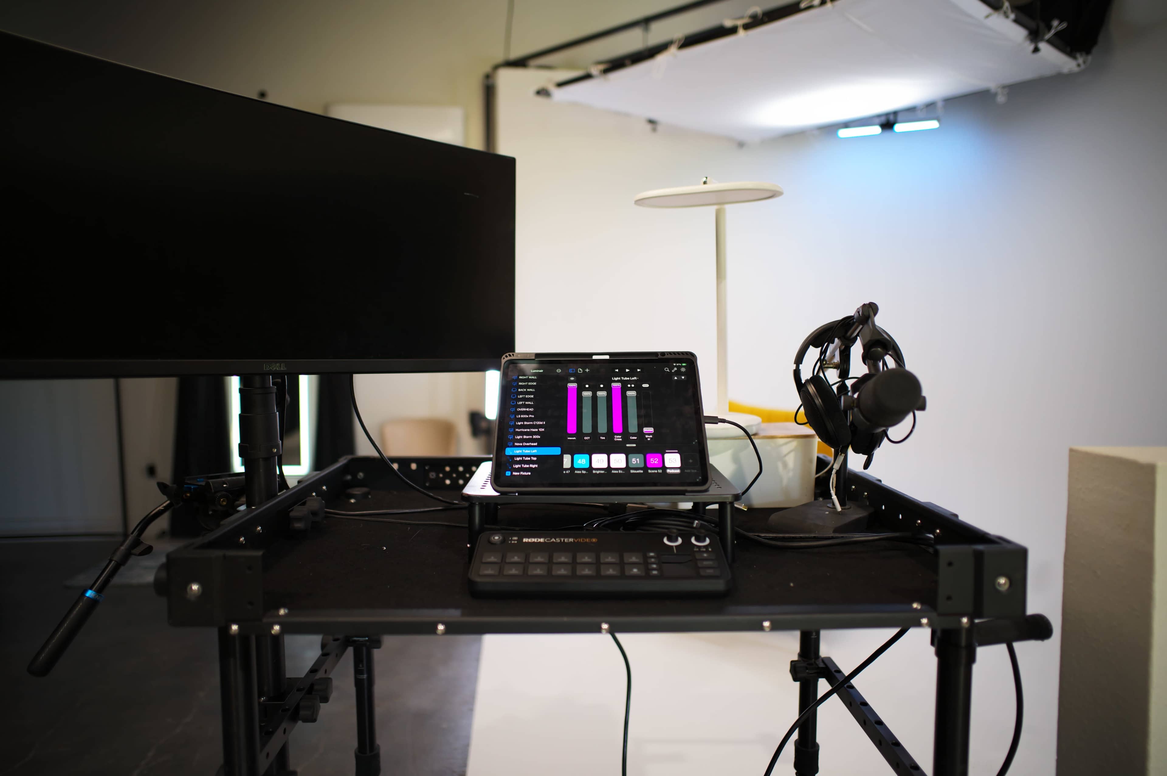 A workstation setup displays a tablet with audio mixing controls, a monitor, and headphones on a black cart in a studio environment.