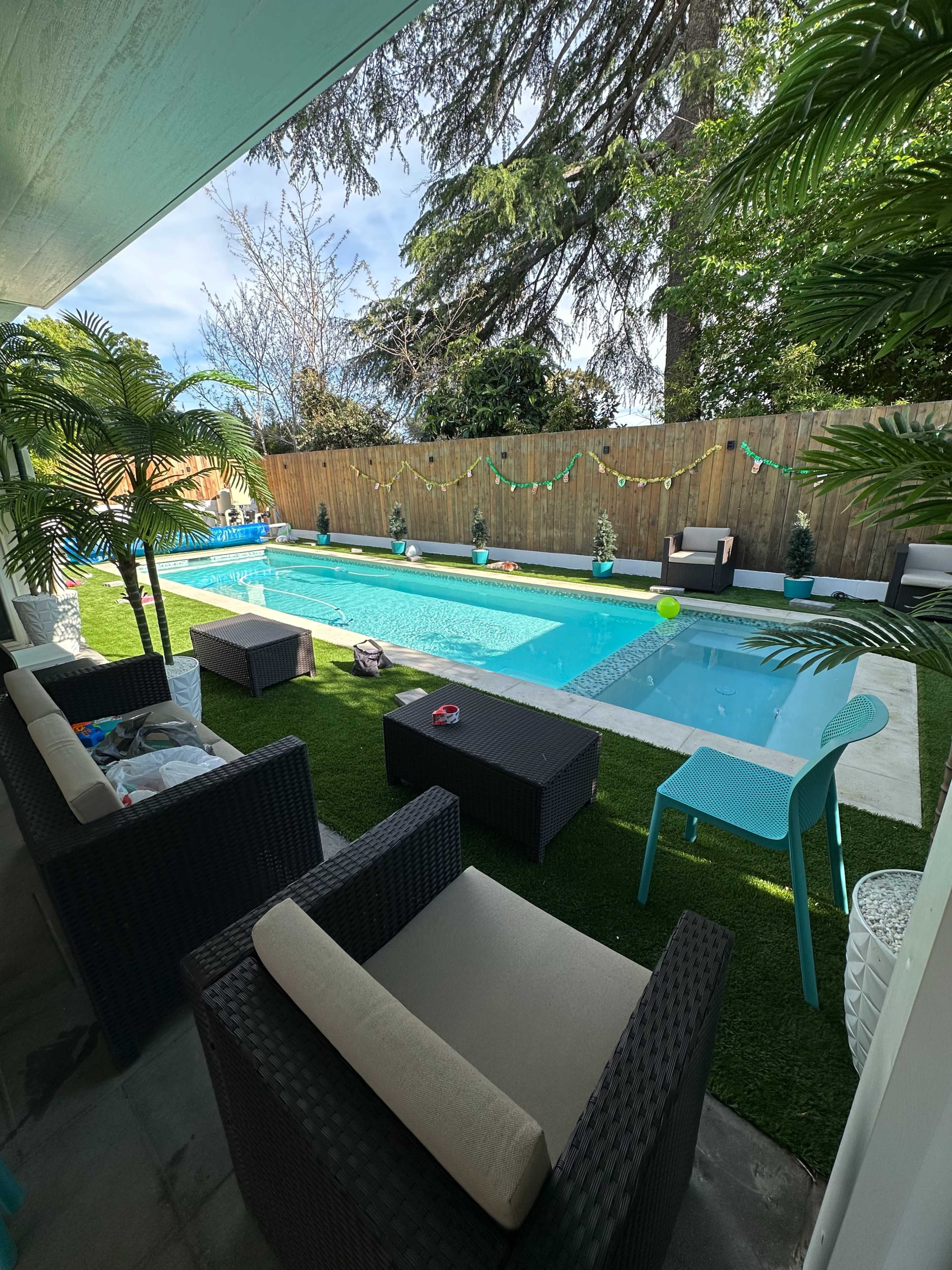 A backyard with a swimming pool surrounded by potted plants and seating areas on a grassy lawn.