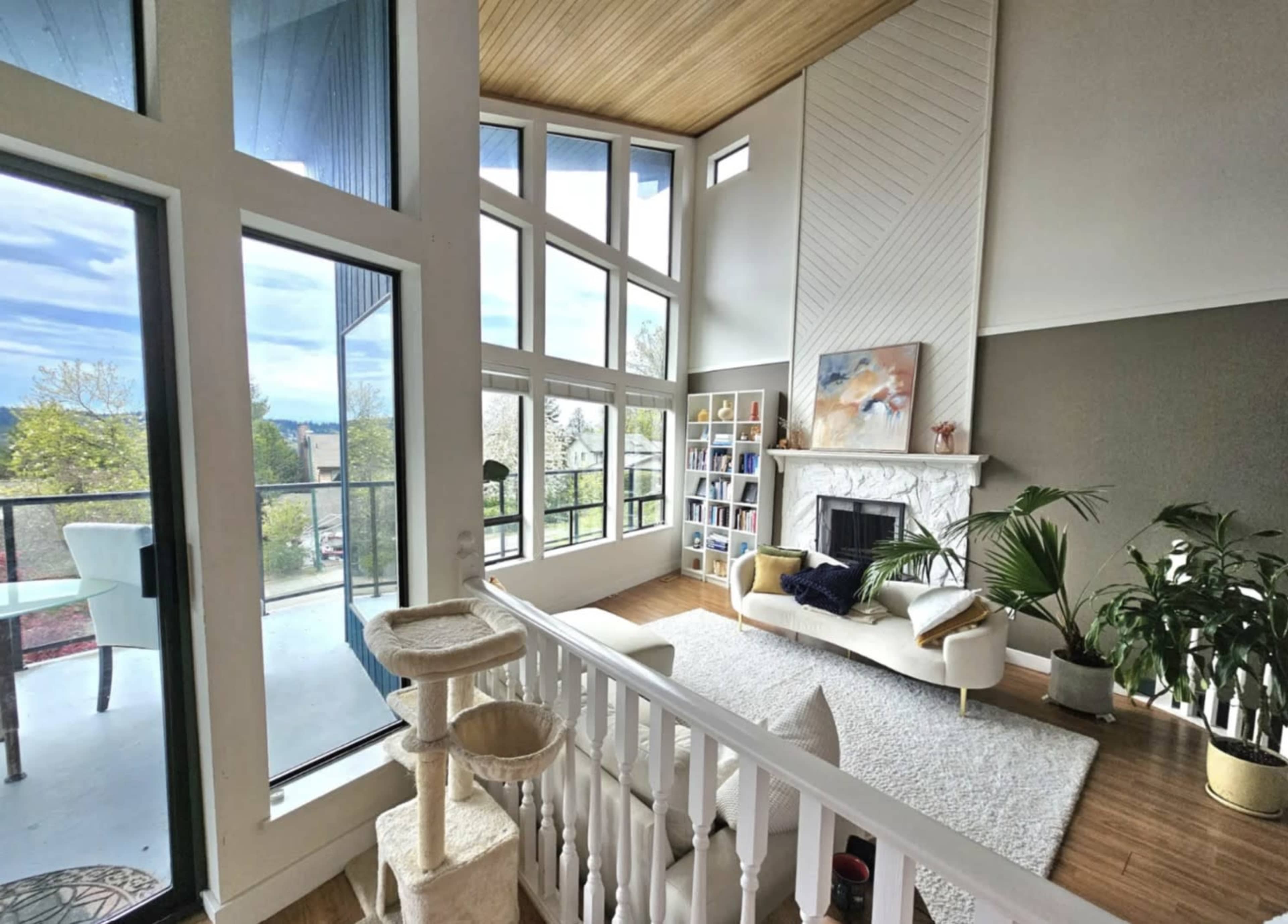 The image shows a modern, open living room with large windows, a fireplace, and a sliding door leading to a balcony.