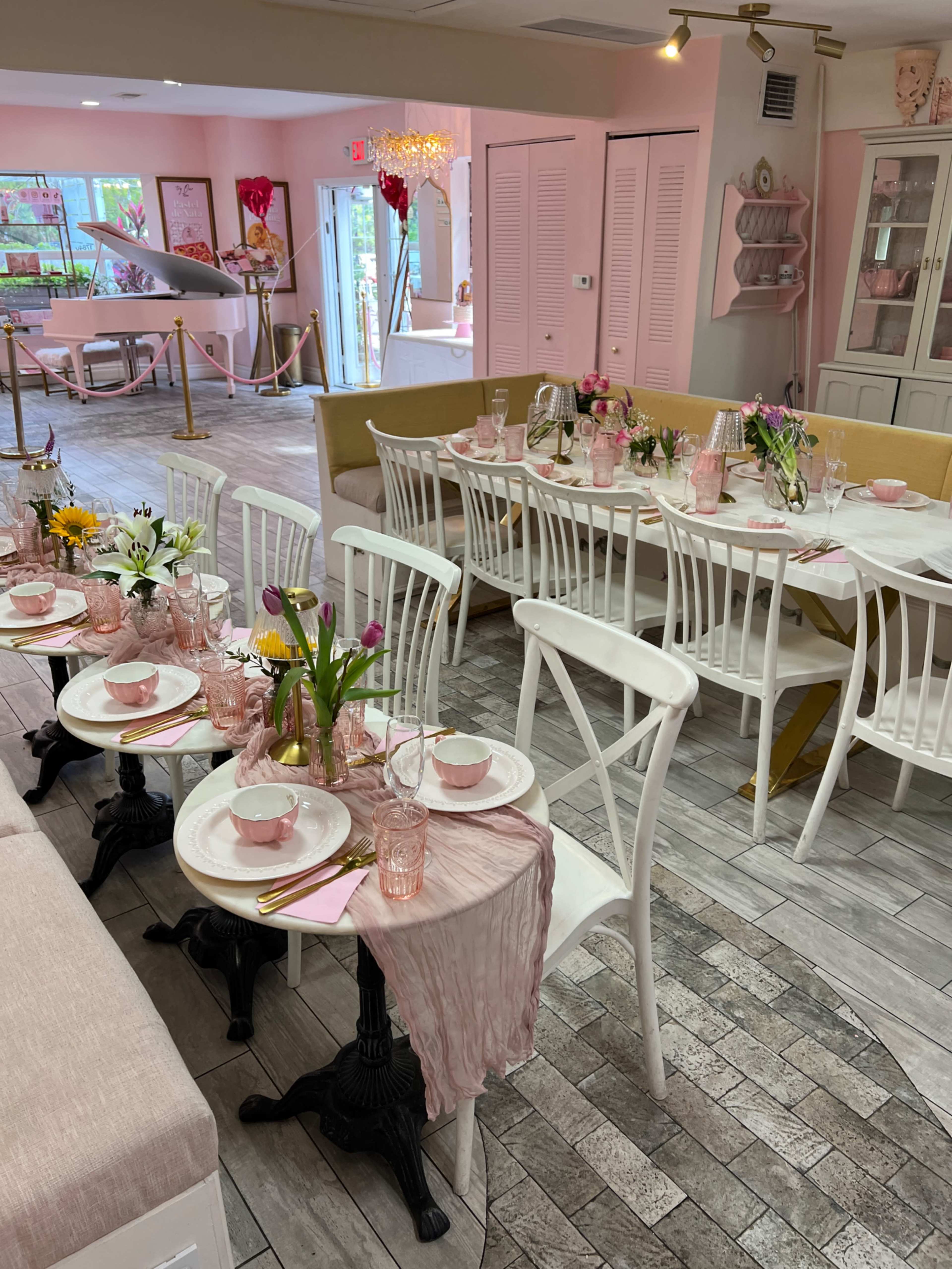 The scene features a bright, pink-themed dining area with tables set with white dishware, colorful flowers, and decorative pink accents.