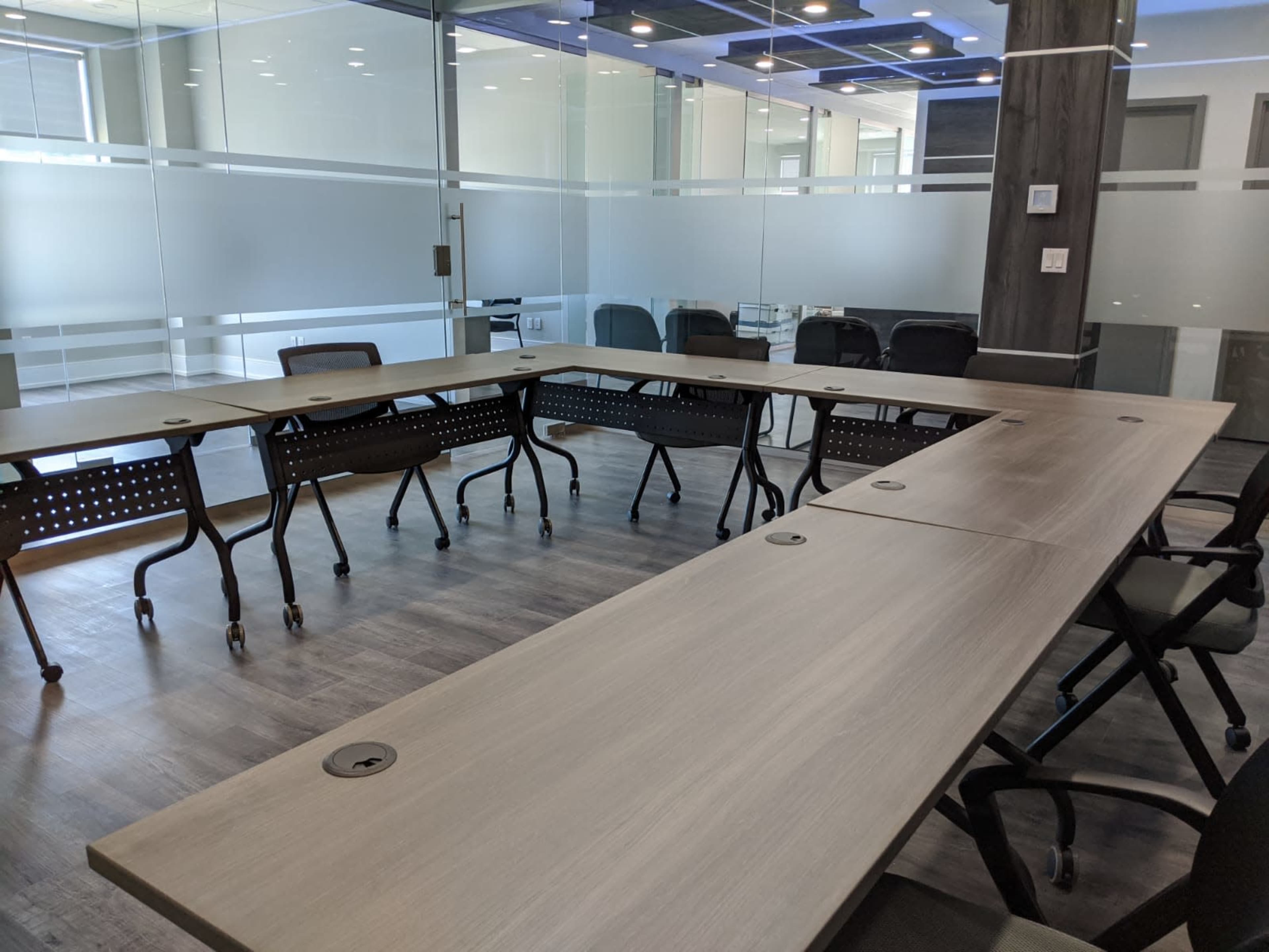 A modern conference room features a large rectangular table surrounded by multiple rolling chairs and a glass wall that provides visibility to adjacent spaces.