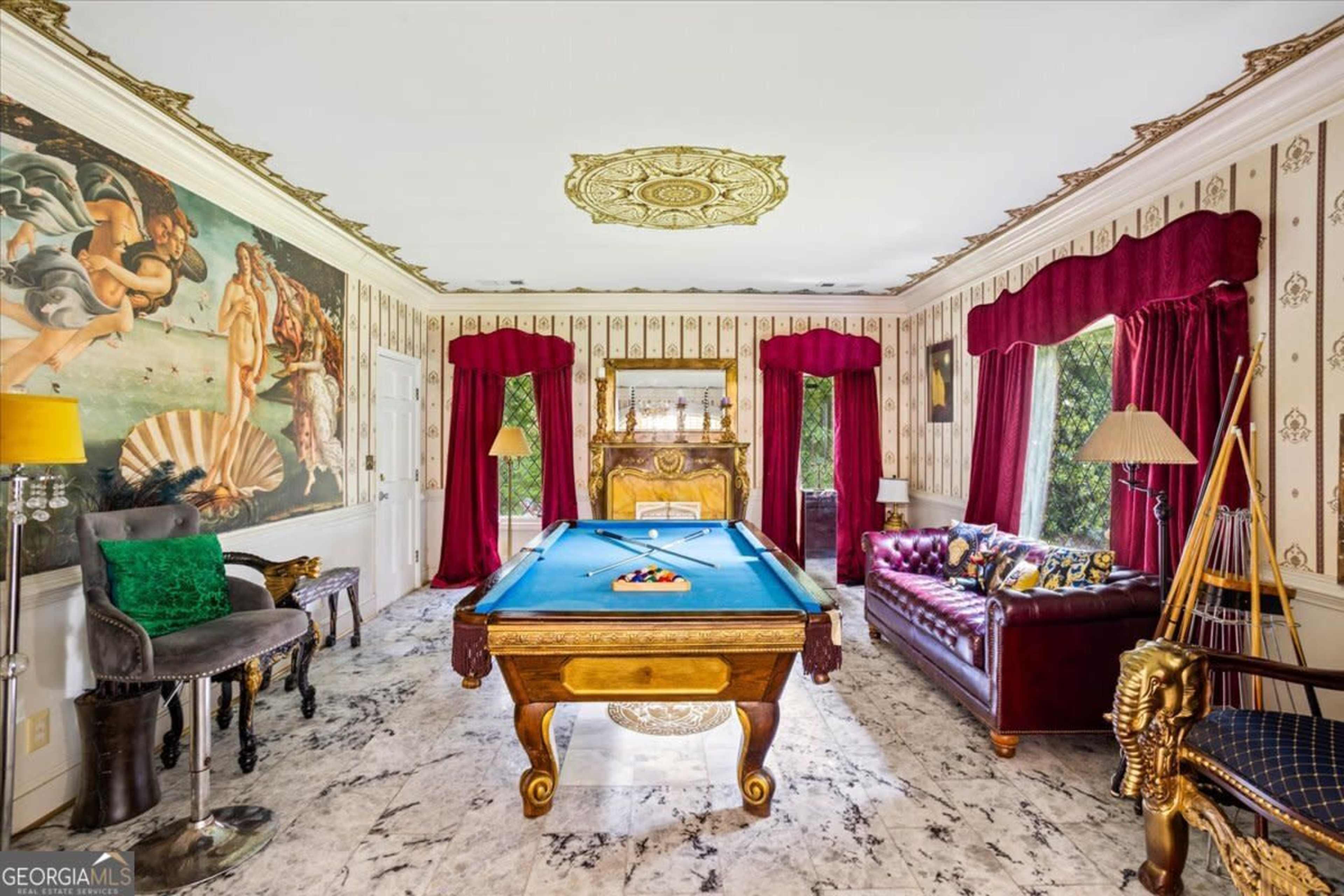 The room features a pool table at its center, surrounded by ornate wallpaper, a leather sofa, and large windows with red drapes.