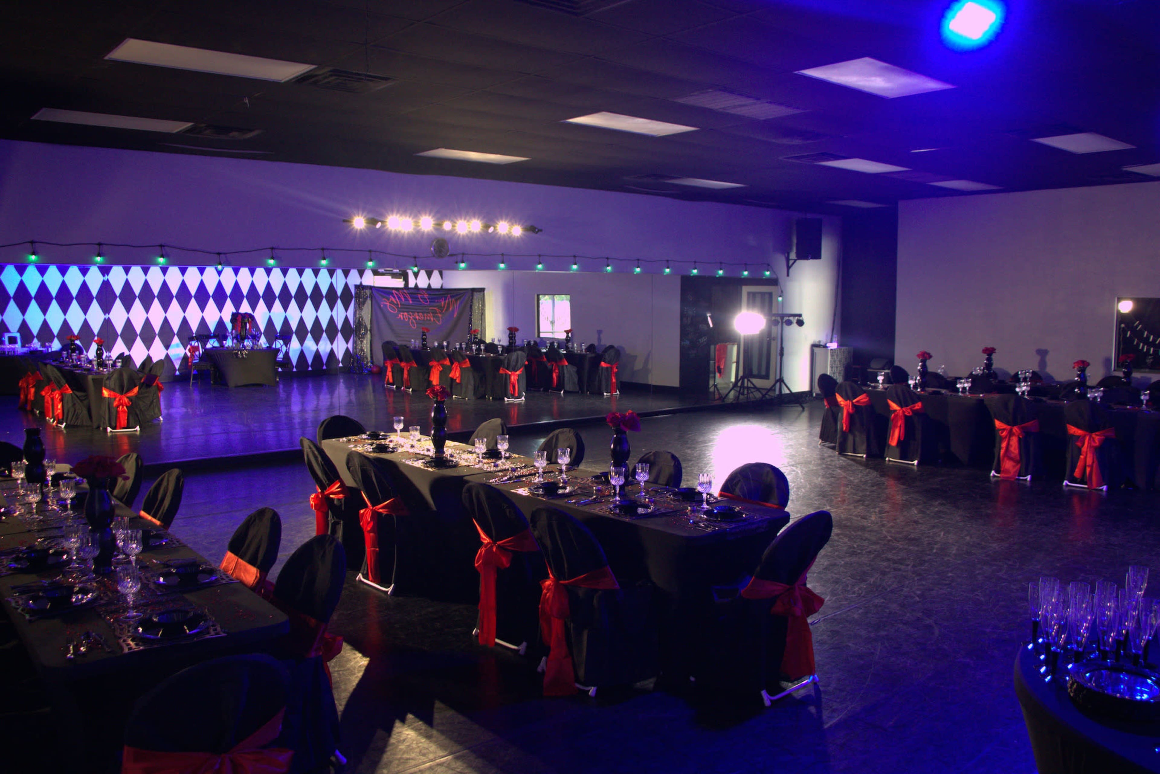 A spacious banquet hall features tables with black covers and red bows, set against a backdrop of checkered walls and vibrant lighting.