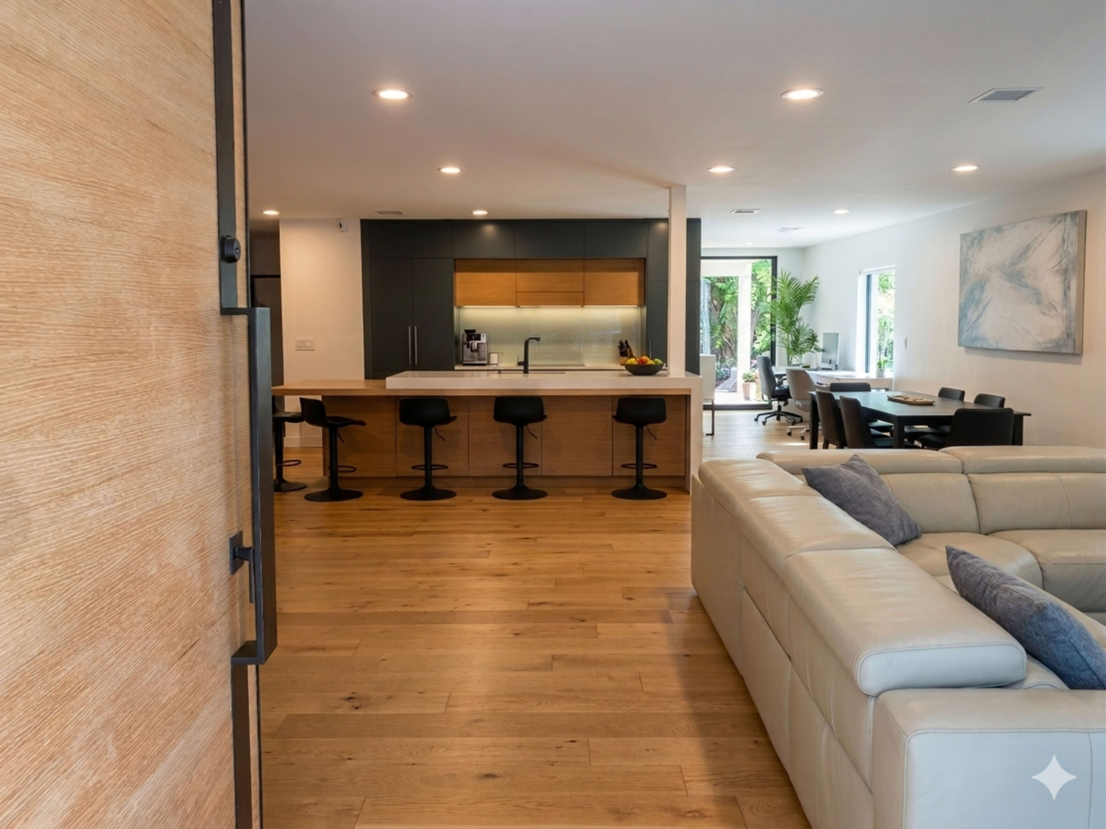 A modern open-concept living space features a kitchen with a large island and bar stools, leading to a dining area with a table and chairs.