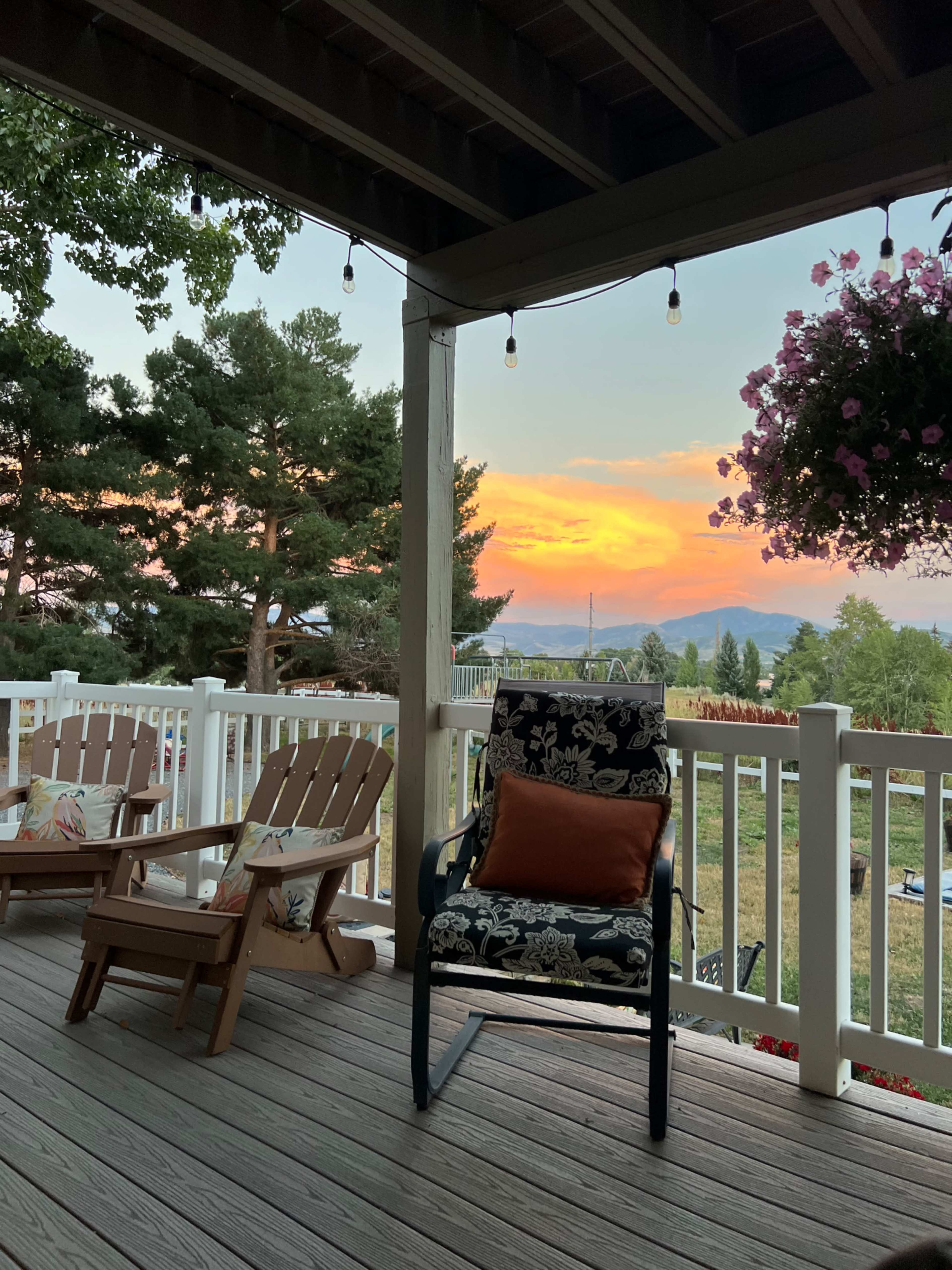 A porch view features two wooden chairs and a floral-patterned chair, overlooking a landscape with trees and a sunset sky.