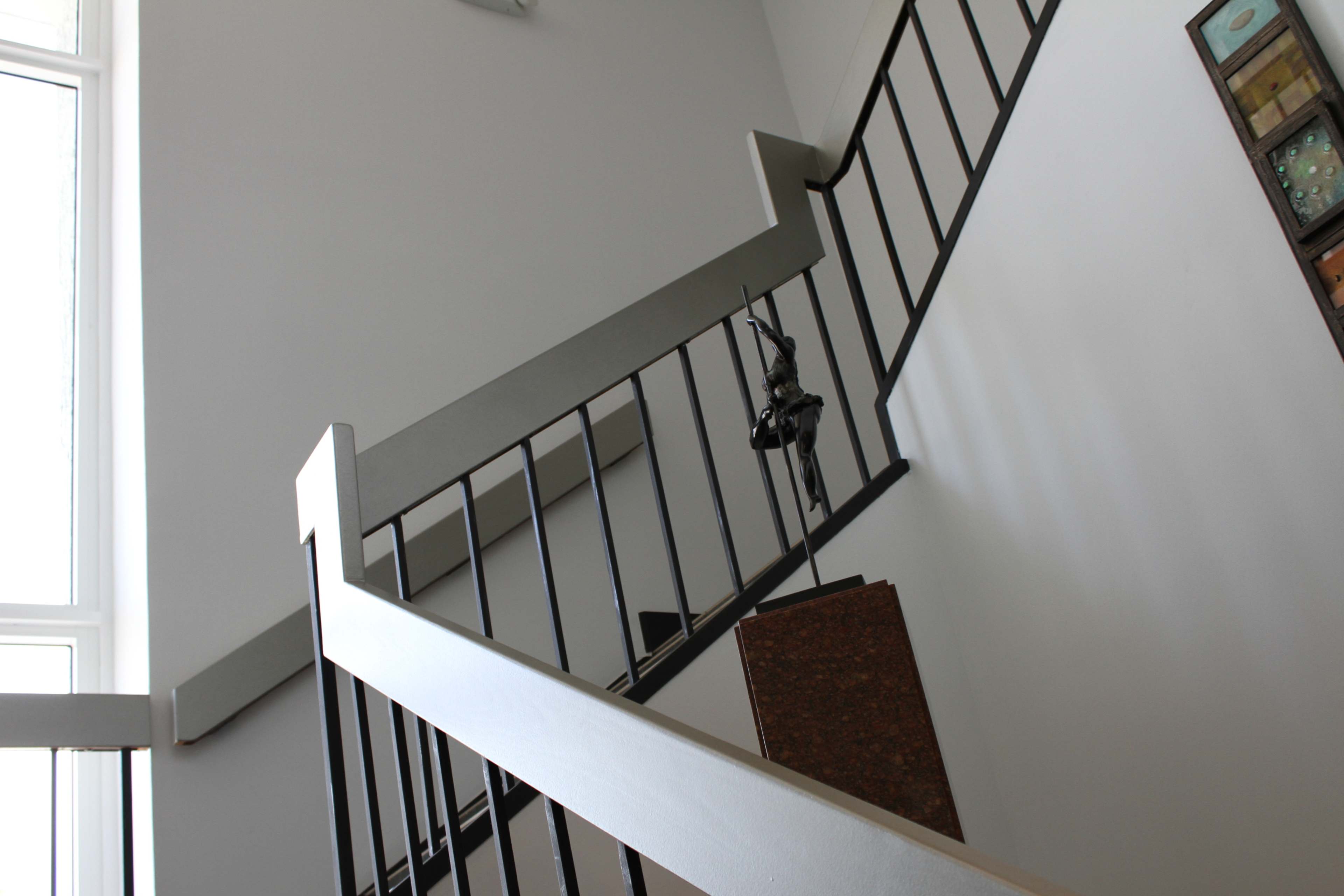 A metal staircase with a railing curves upwards, leading to a landing and a wall adorned with artwork.