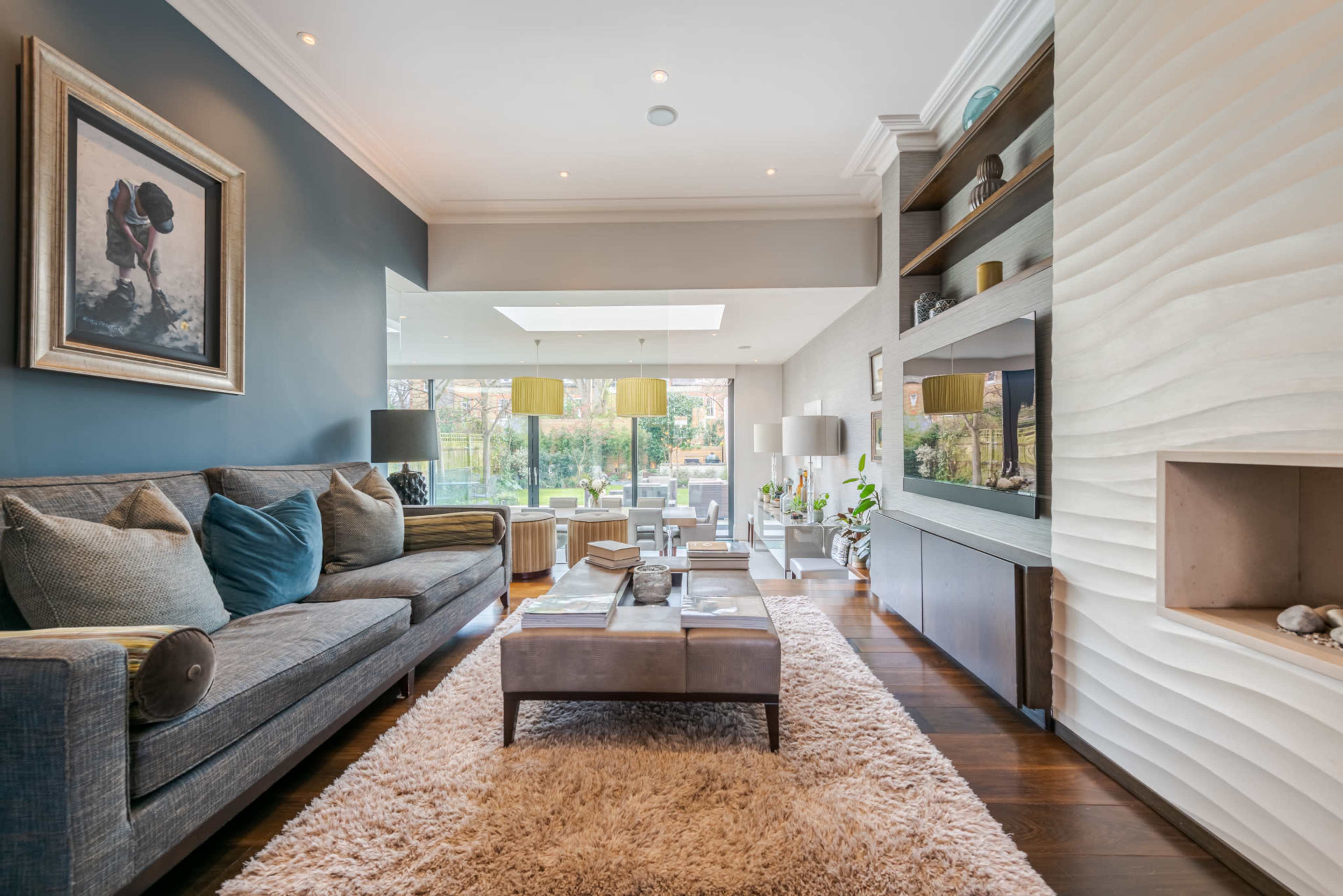 The image shows a modern living room with a gray sofa, a coffee table, and decorative accents, featuring large windows that allow natural light to fill the space.