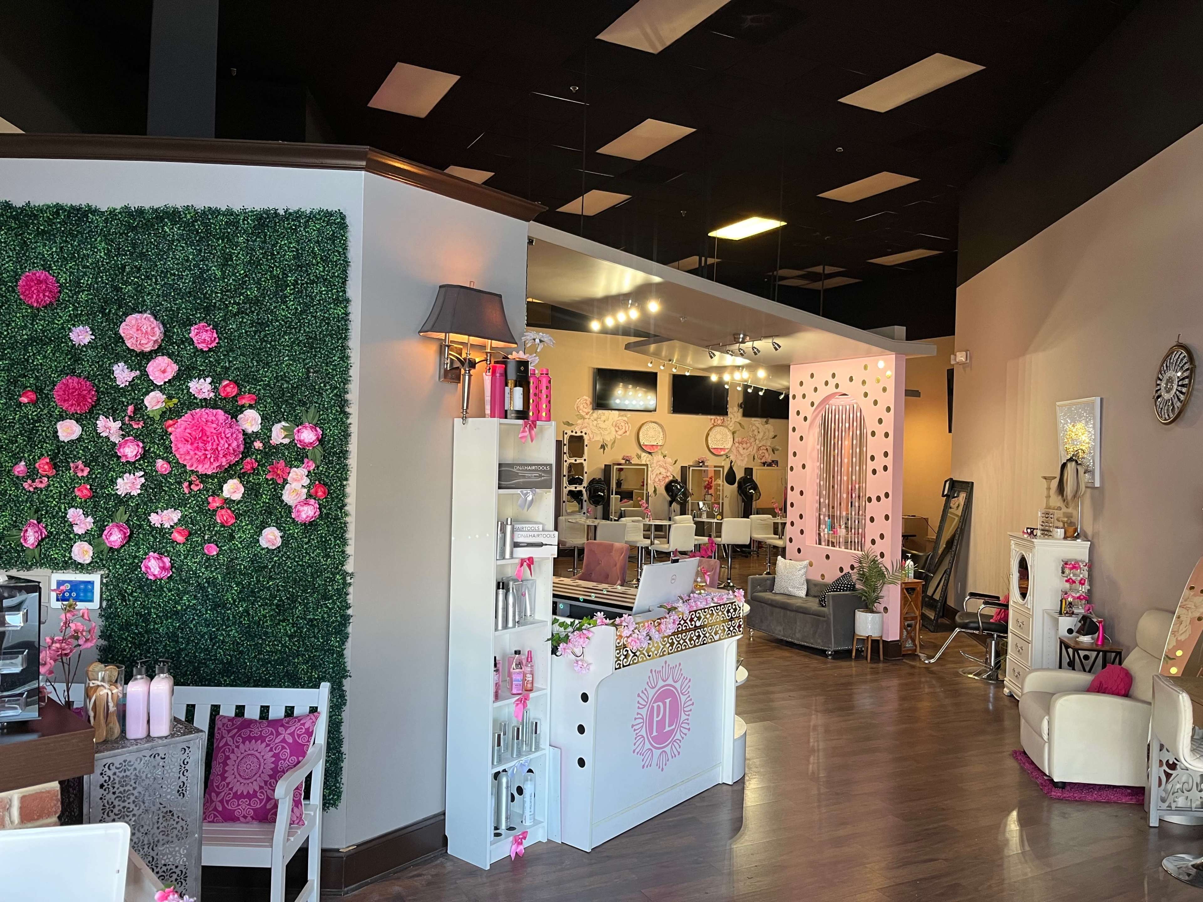 A beauty salon interior with a decorated green wall, stylish seating areas, and a reception desk adorned with pink accents.