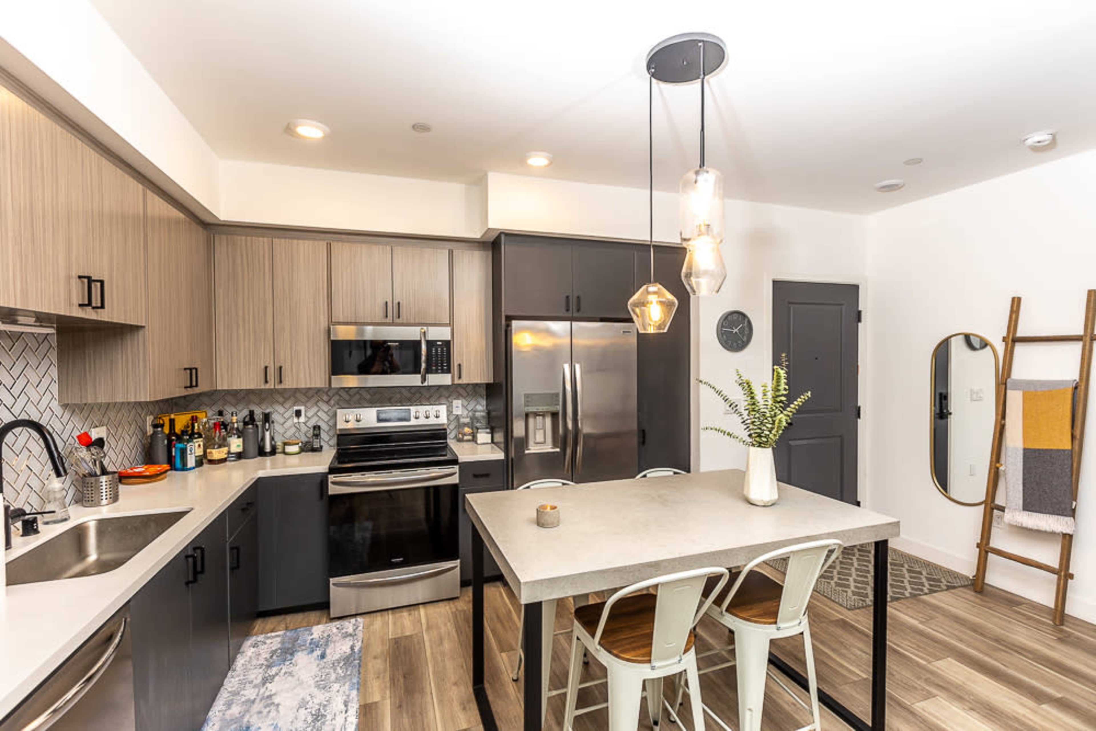 A modern kitchen with wood and gray cabinetry, stainless steel appliances, a central island with seating, and decorative elements on the countertop.