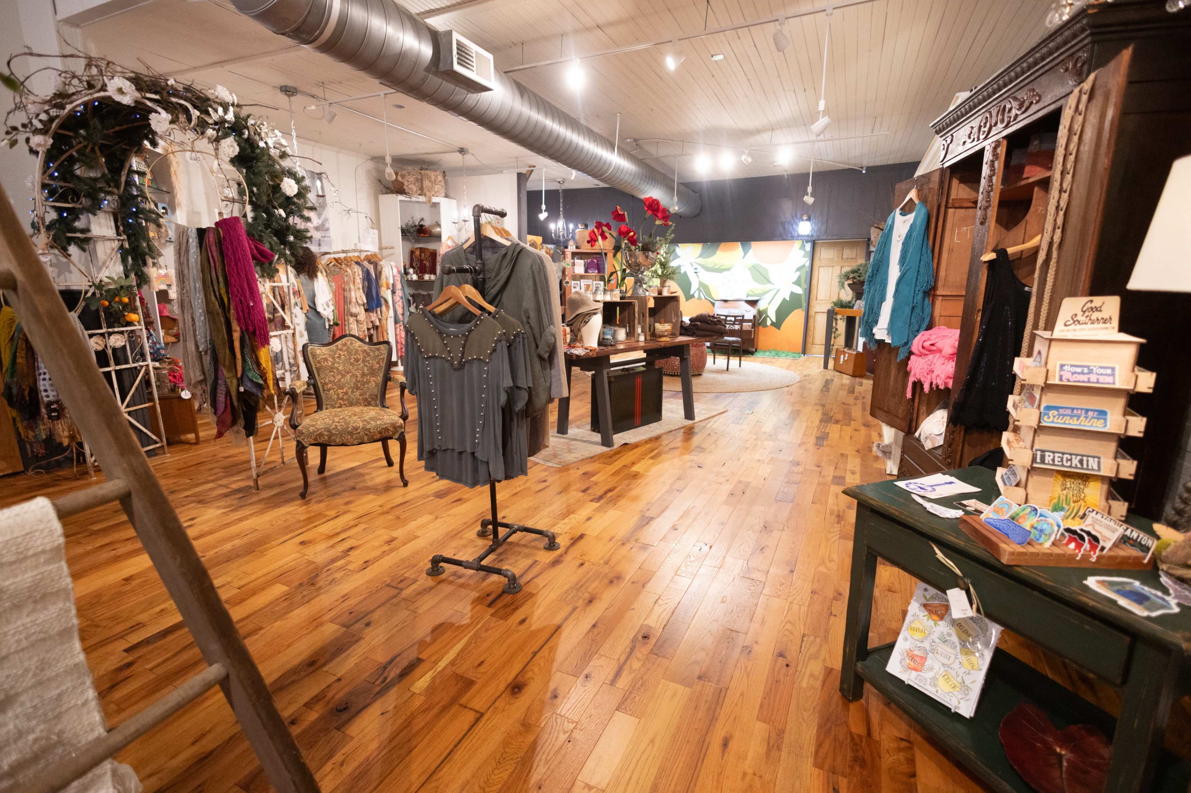 The image shows a cozy boutique filled with clothing racks, decorative furniture, and wooden flooring, illuminated by soft overhead lighting.