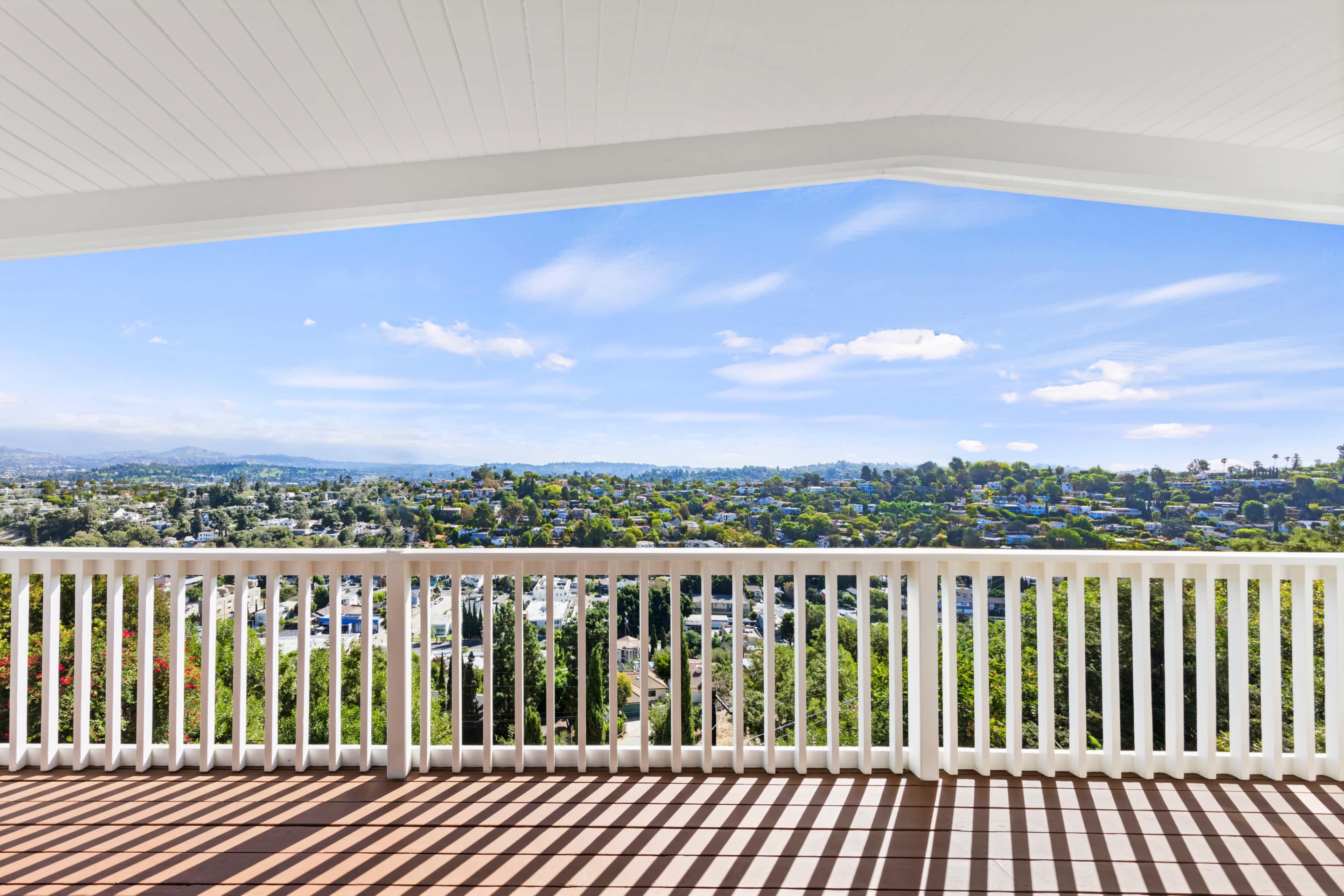 A spacious balcony offers a view of a lush, green landscape under a clear blue sky.