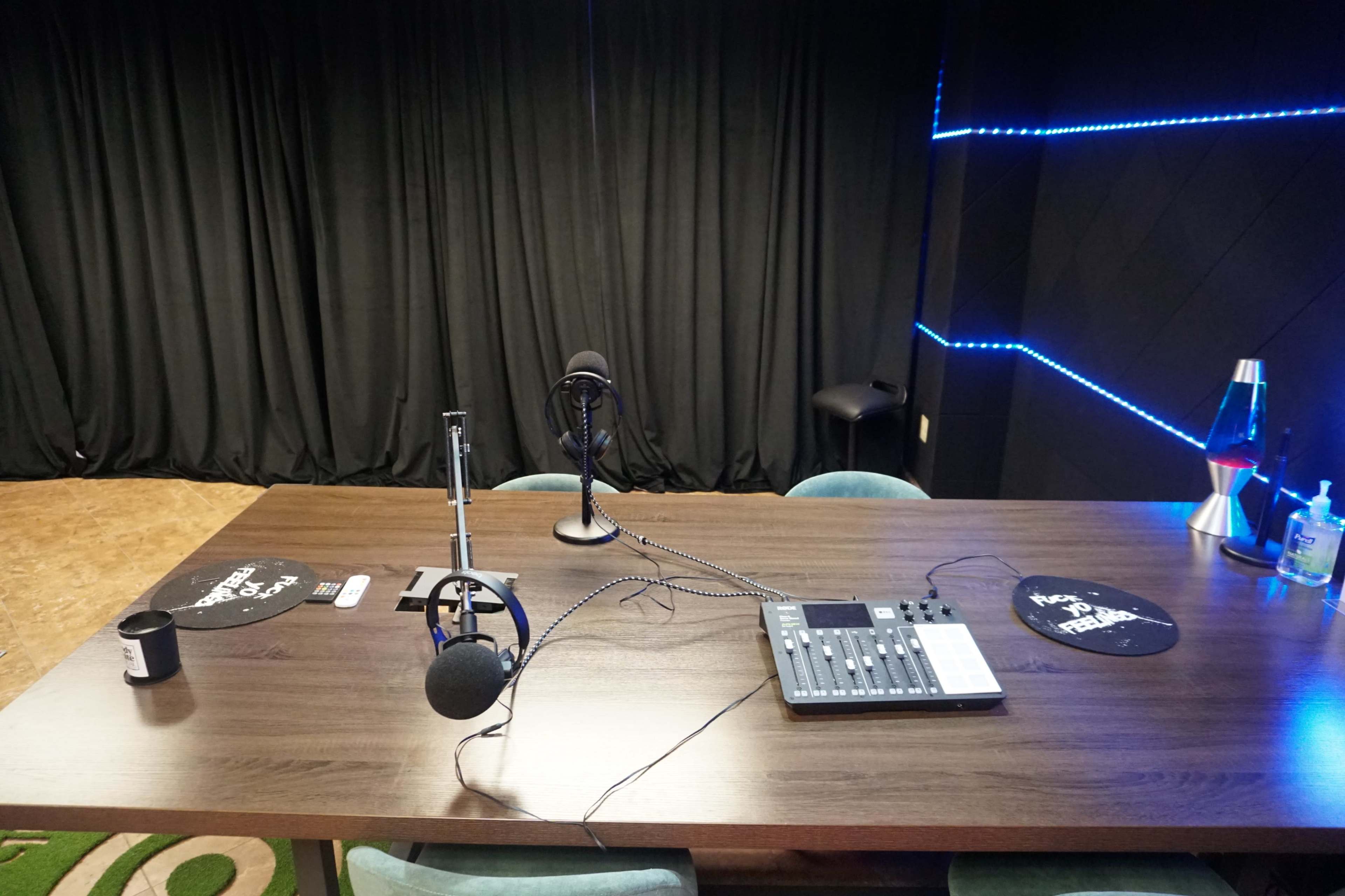 A podcast recording setup featuring a wooden table with microphones, a sound mixer, and black curtains in the background.