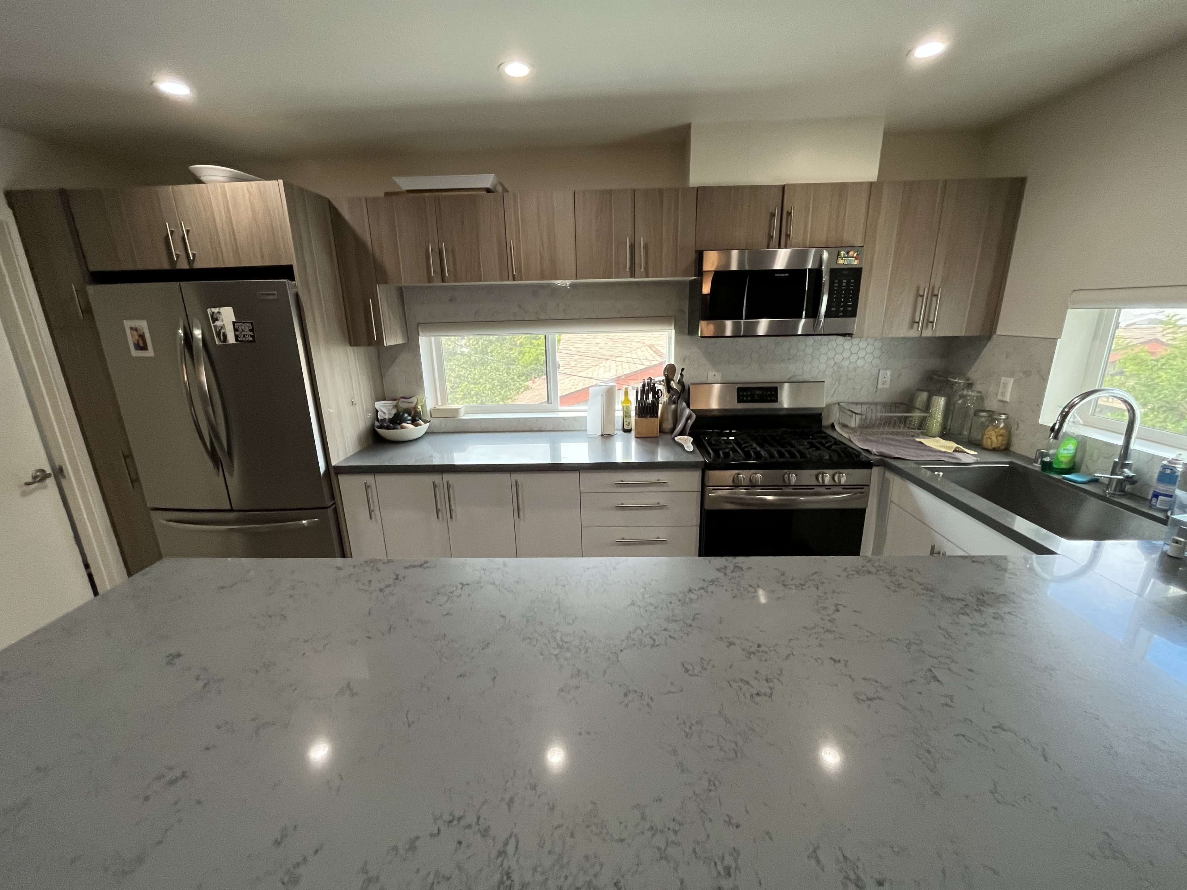 The image shows a modern kitchen with wooden cabinetry, stainless steel appliances, and a gray marble countertop.