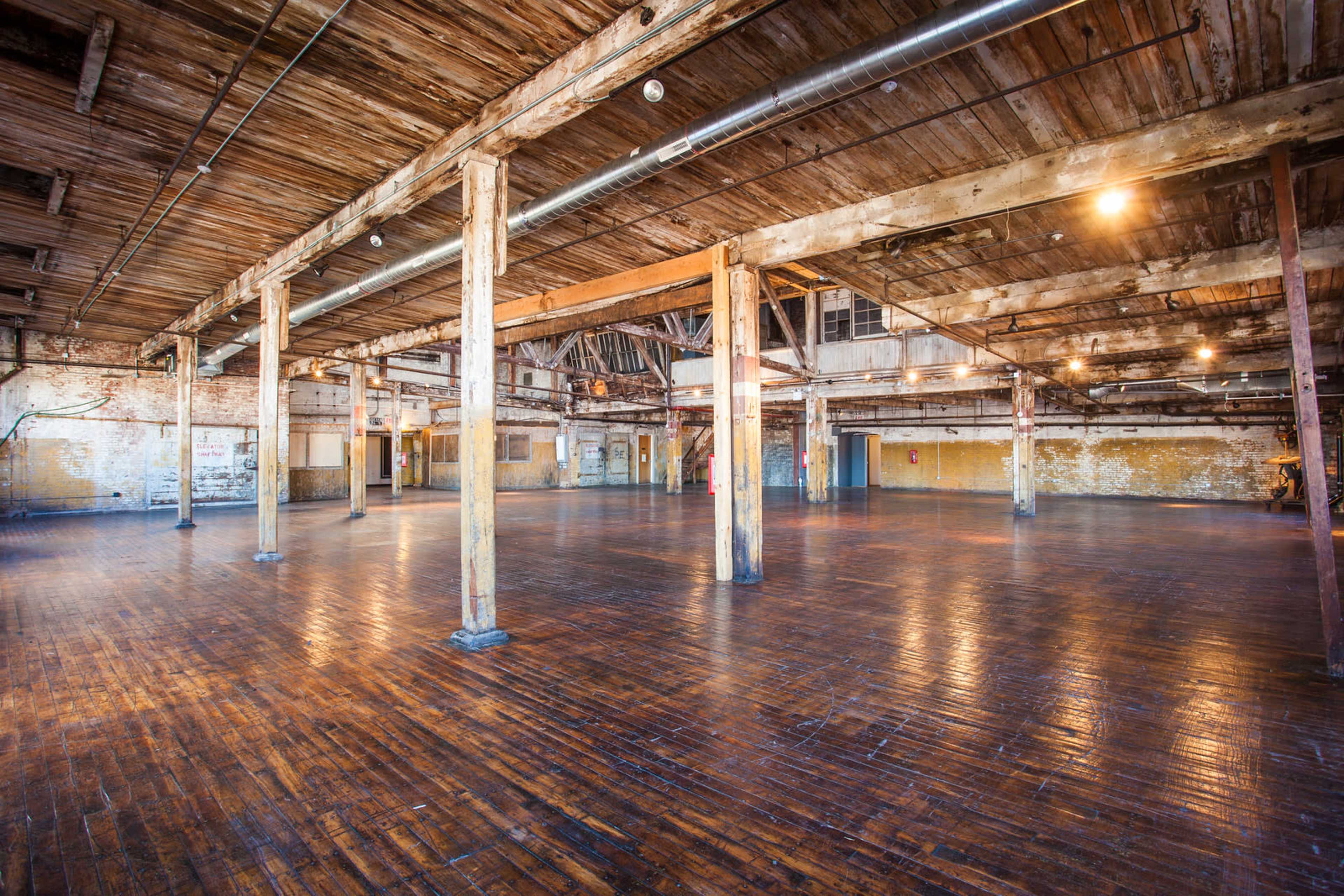 A spacious, empty industrial interior with wooden floors and exposed beams.