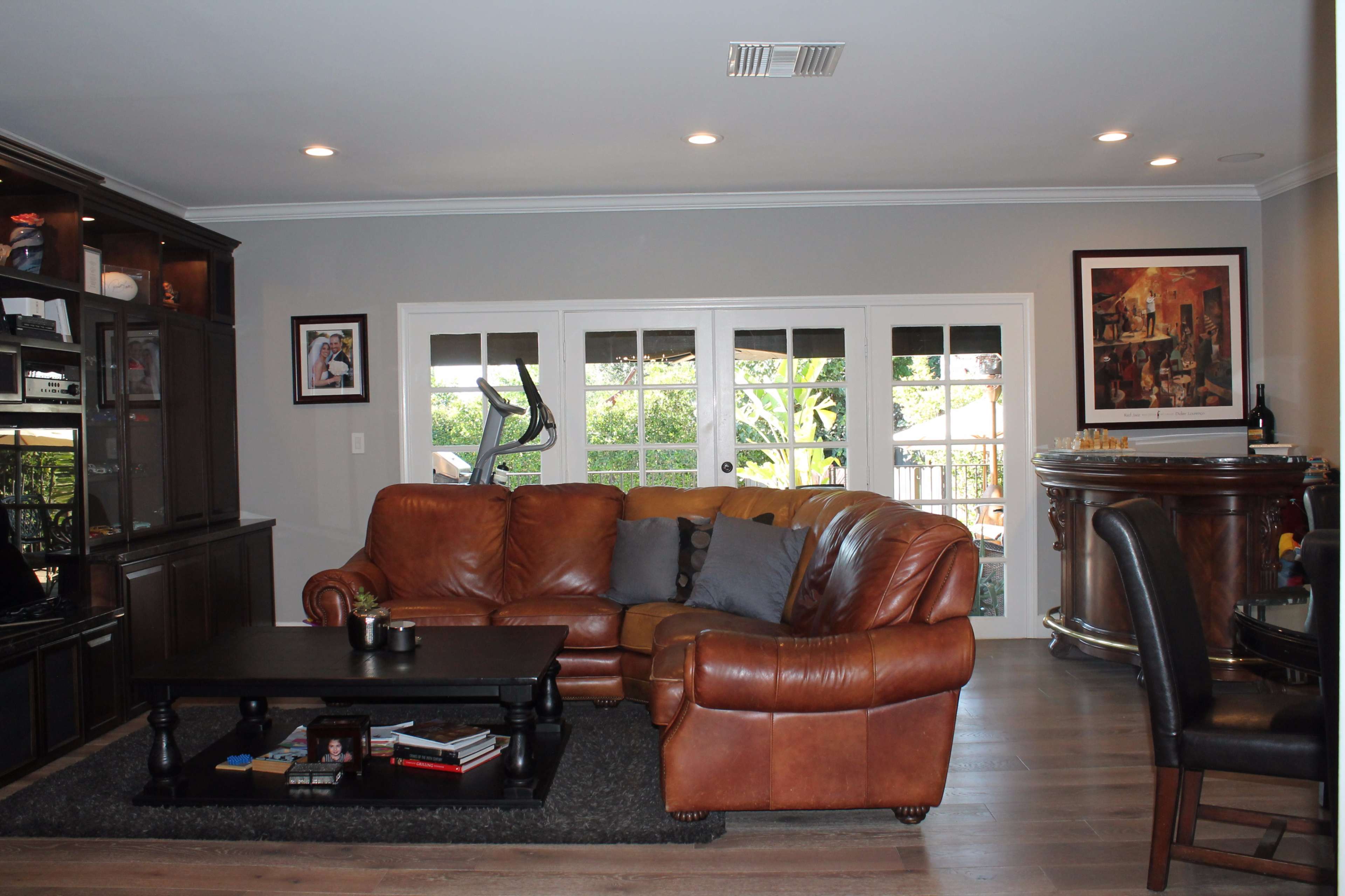 The living room features a brown leather sofa, a black coffee table, and large windows that provide a view of the outdoor area.