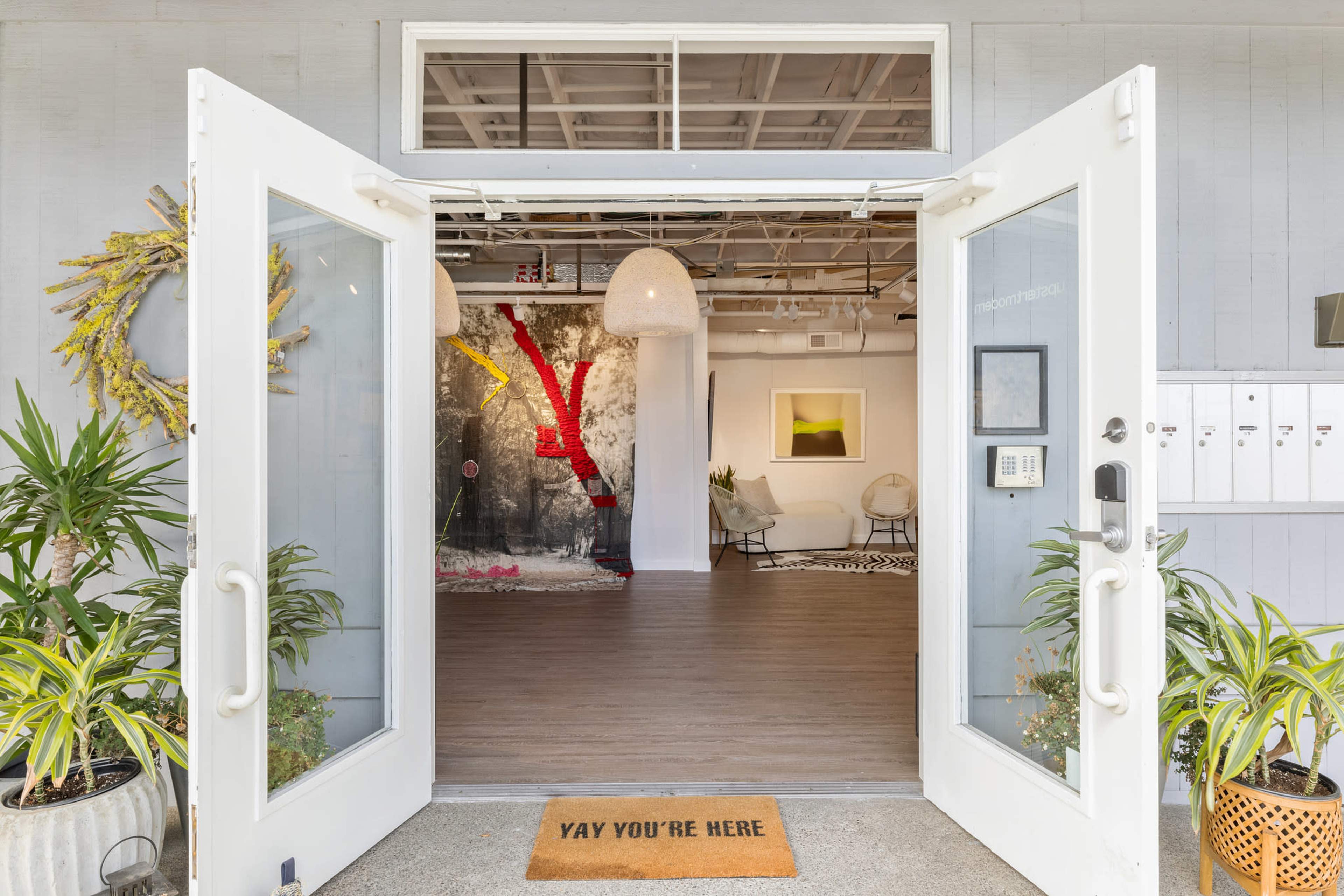 A welcoming entrance with double doors open, leading into a modern interior featuring artwork and plants.