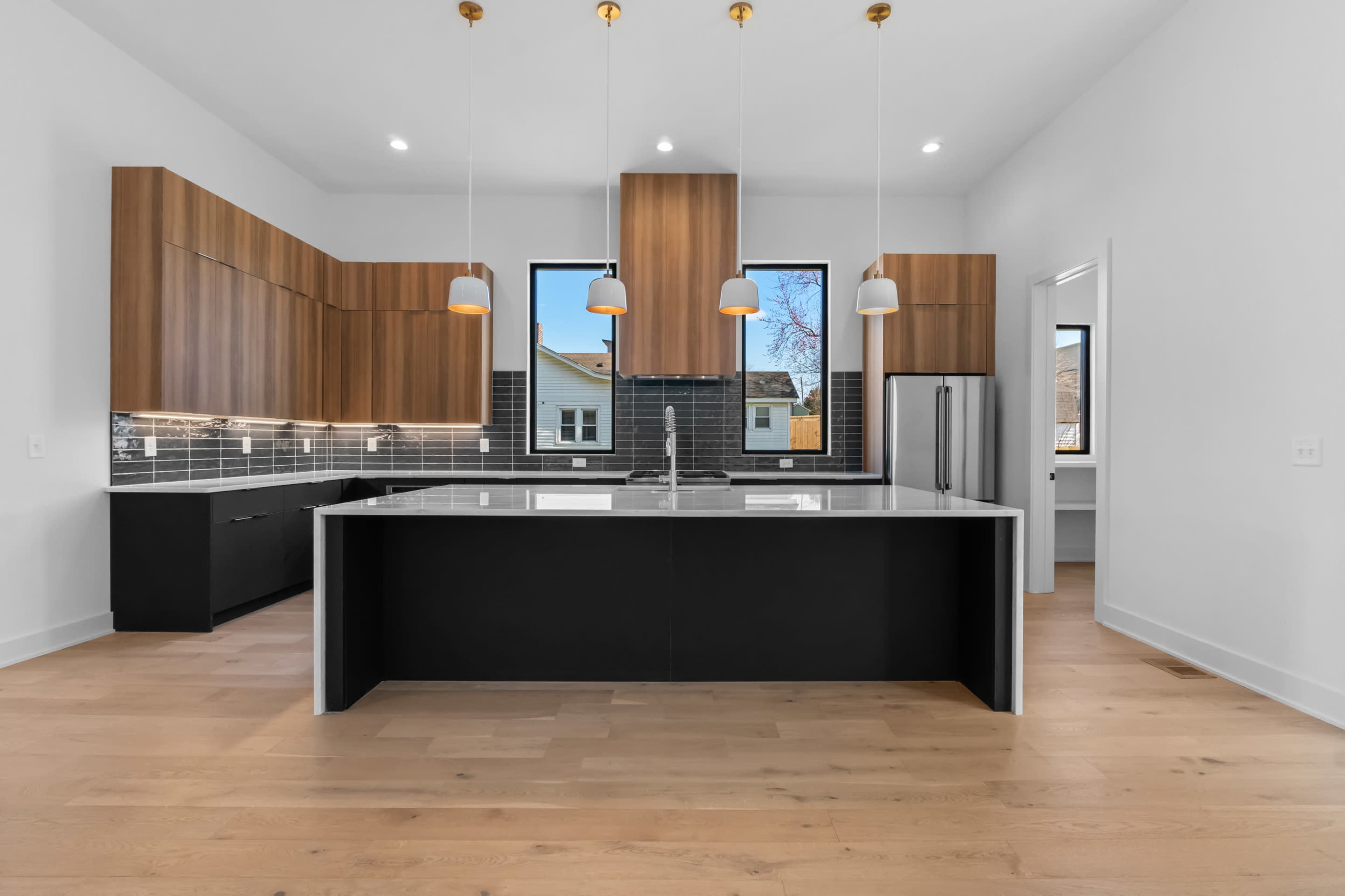 A modern kitchen features wooden cabinets, a large island with a dark base, and pendant lighting above.