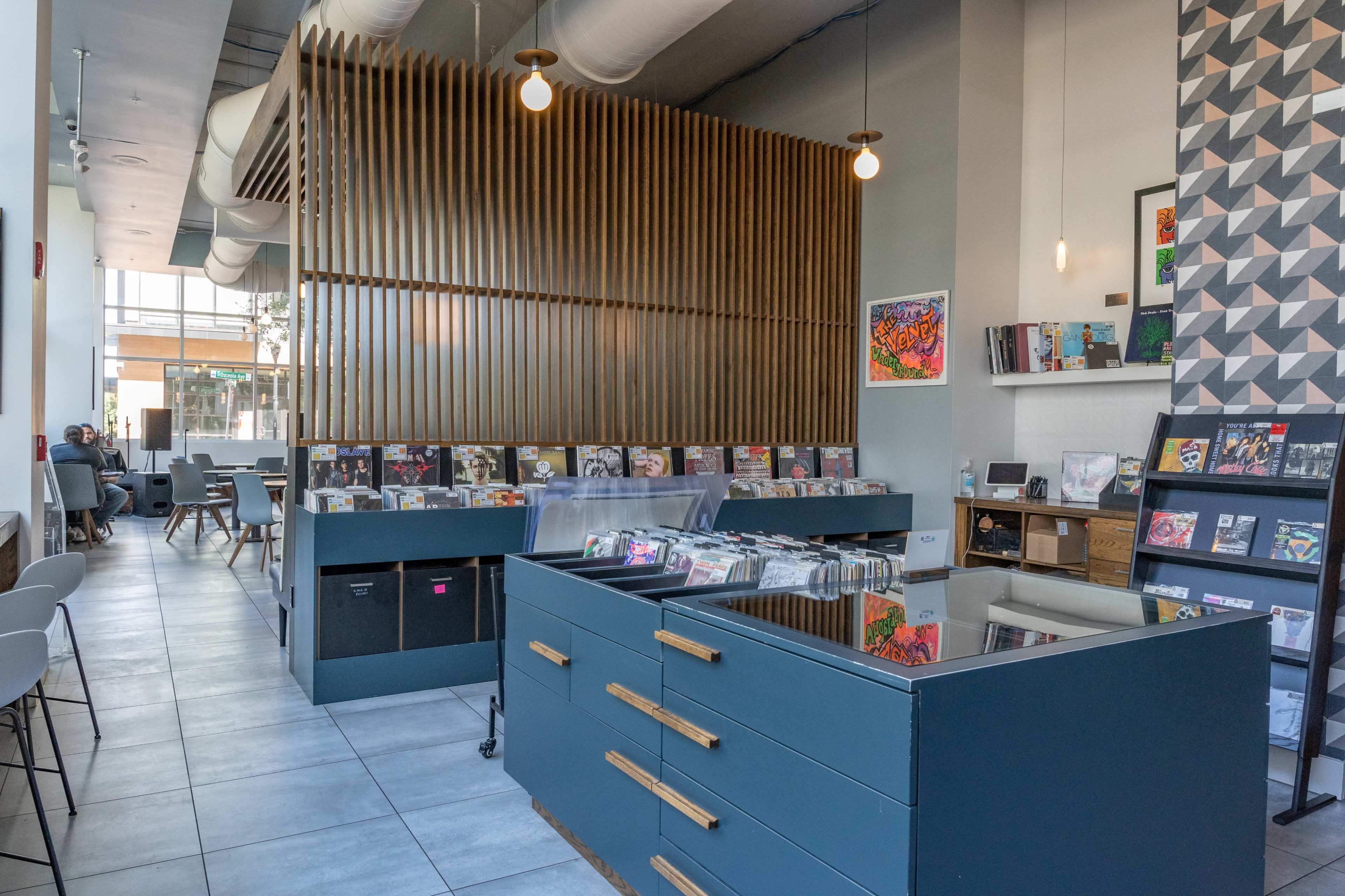 The interior of a modern café features a sleek counter displaying various vinyl records and a wooden partition in the background.