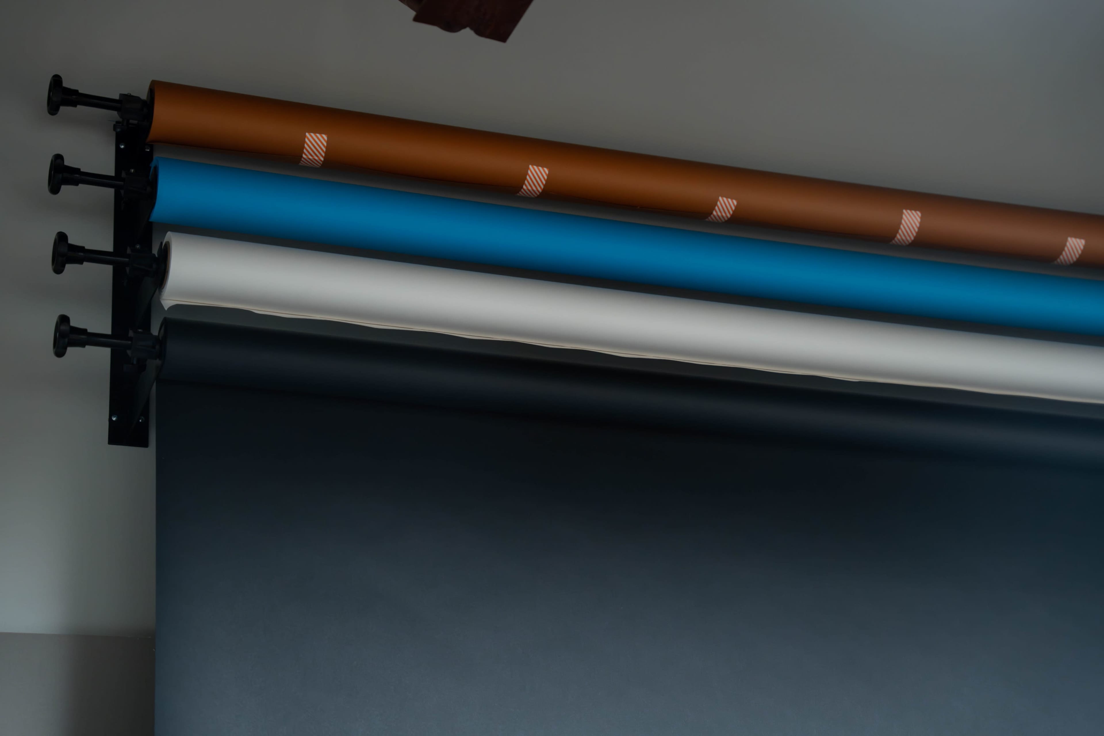 The image shows several rolls of colored backdrop paper stacked on a rod, including shades of brown, blue, white, and black.