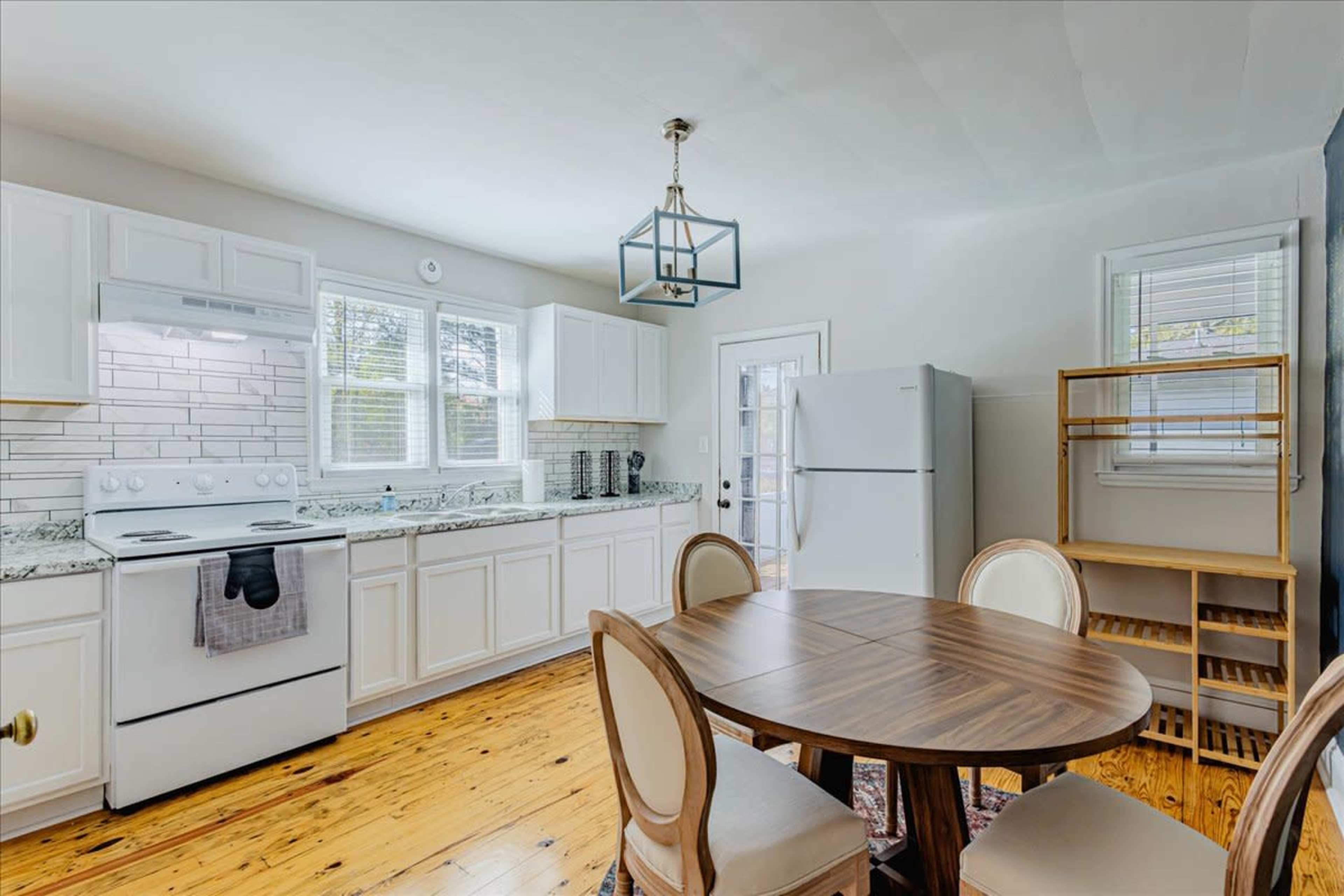 A modern kitchen features white cabinets, a tile backsplash, and a round dining table with four chairs.