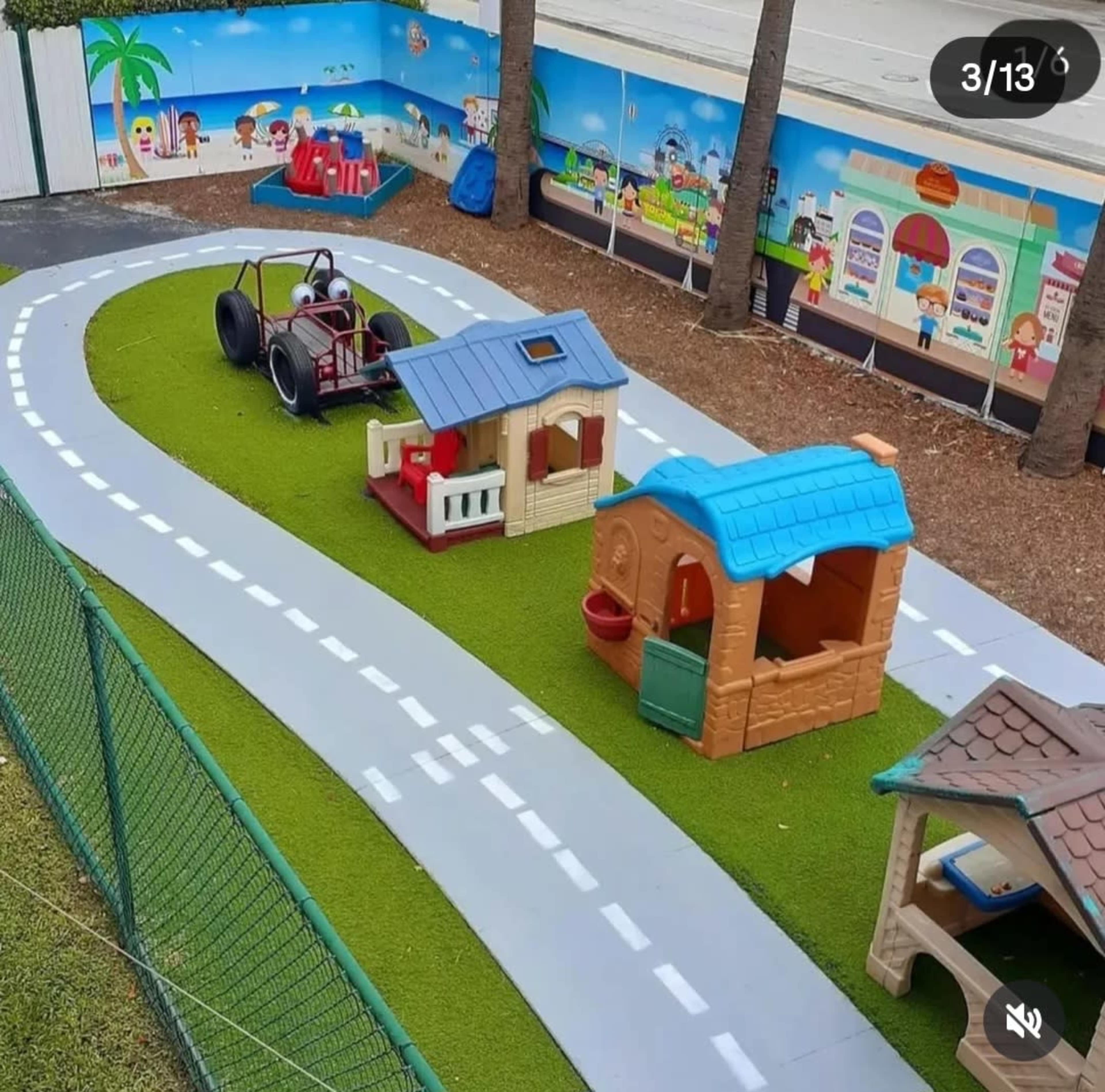 The image shows a children's playground with a toy tractor on a grassy surface, surrounded by playhouses and a winding pathway.