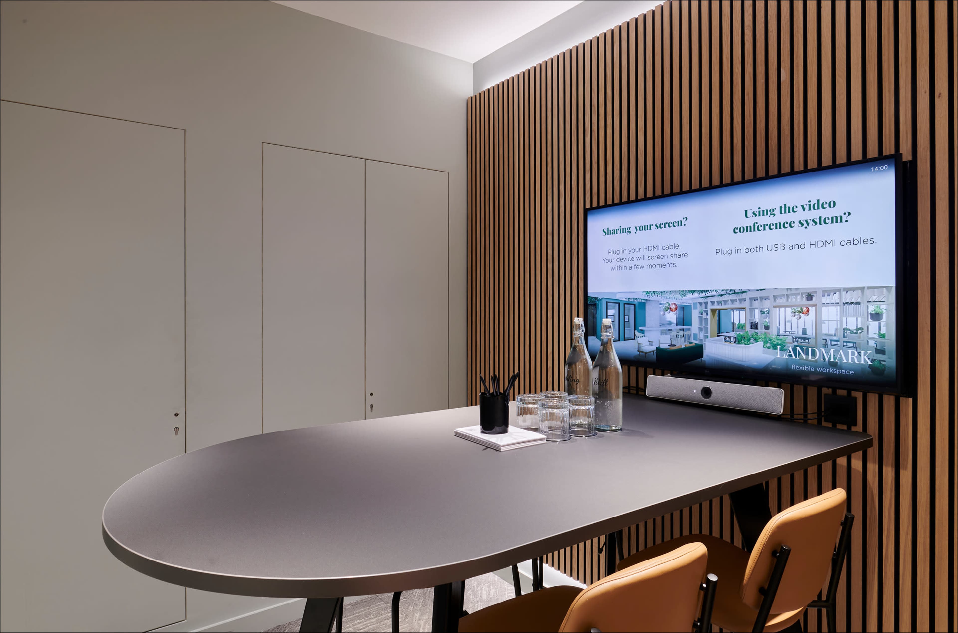 A meeting room features a large table, a television displaying instructions for video conferencing, and a backdrop of wooden paneling.