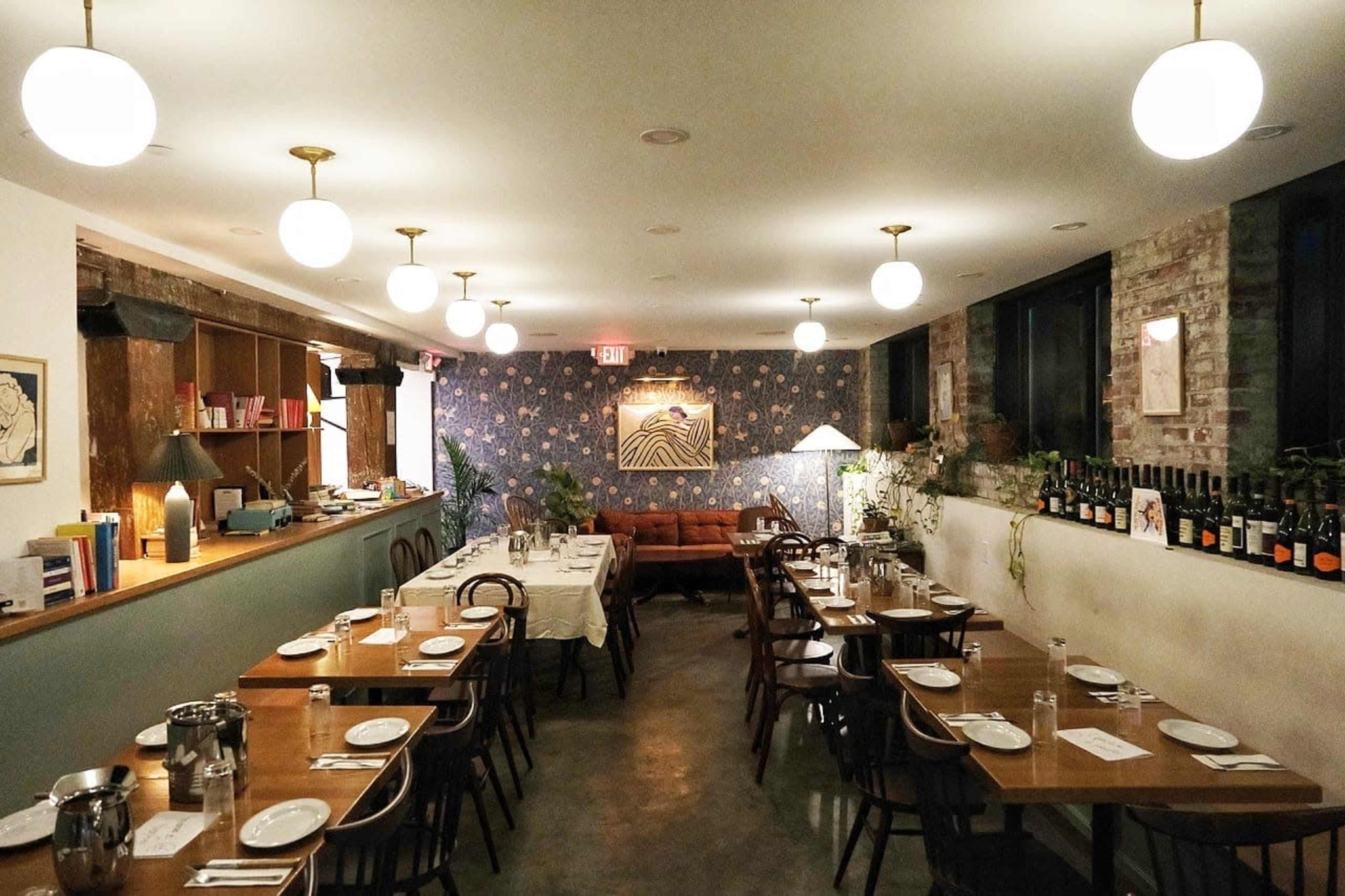 The image shows a well-lit restaurant interior with wooden dining tables, chairs, and decorative wall art, complemented by soft pendant lighting.