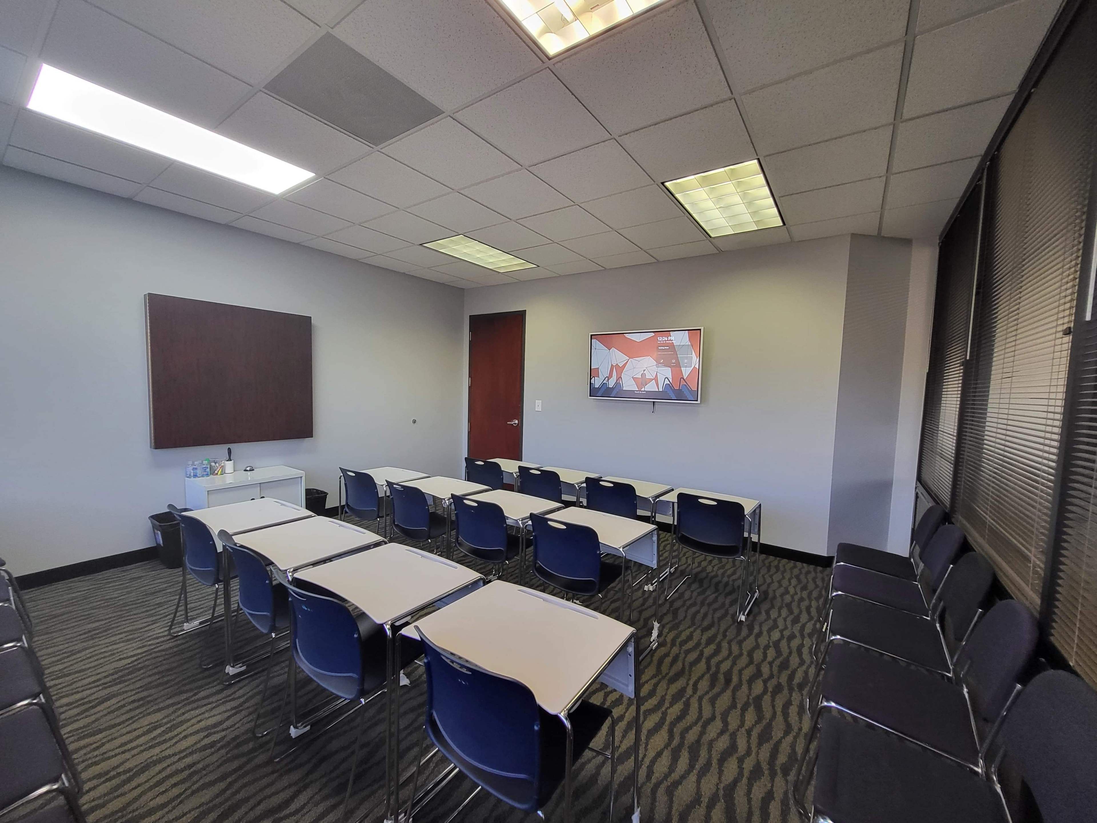 A classroom setup with several desks arranged in rows and a wall-mounted screen displaying a graphic on one side.