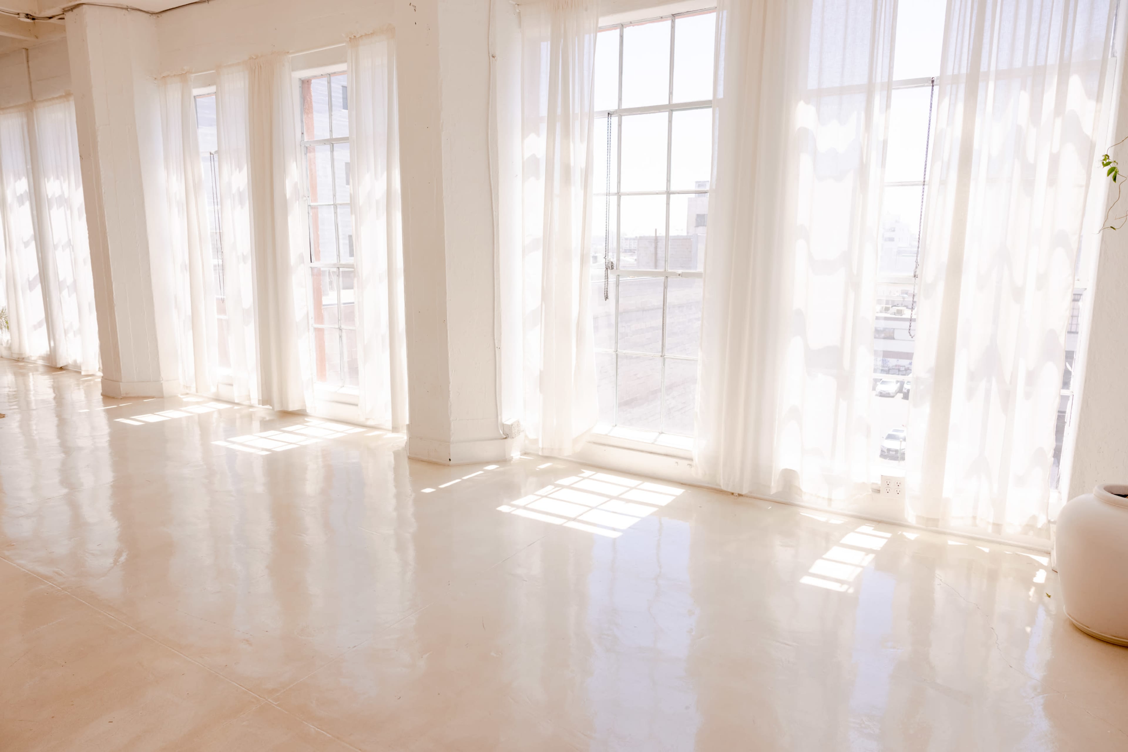 A bright, airy room with large windows covered by sheer curtains, illuminating a polished floor.