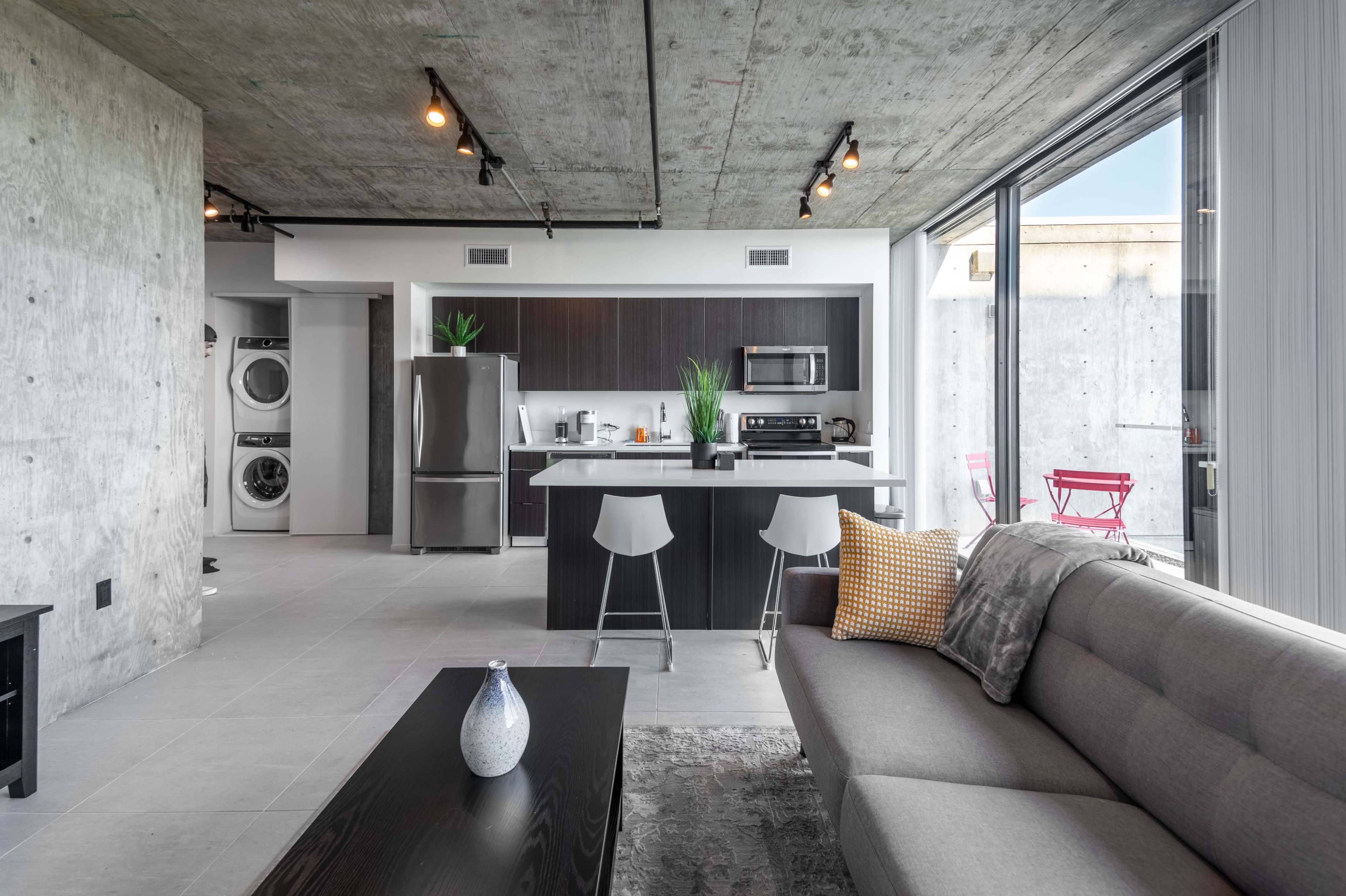 A modern open-concept living space featuring a sleek kitchen with stainless steel appliances, a gray sofa, and a dining area with contemporary chairs.