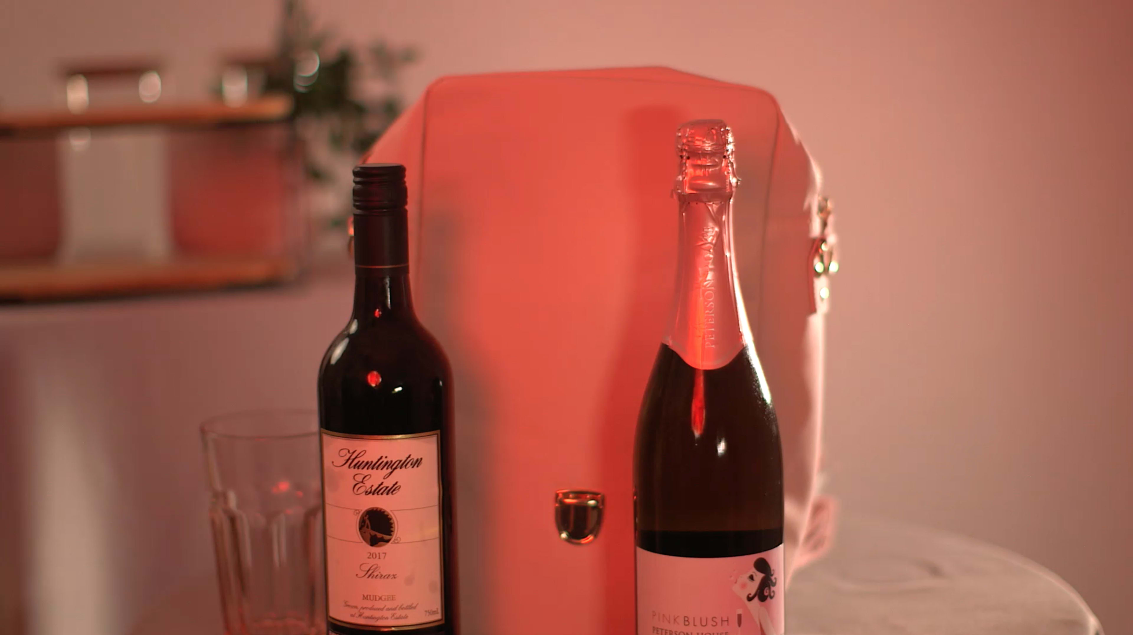 A wine bottle and a sparkling wine bottle are placed next to a pink backpack on a table.