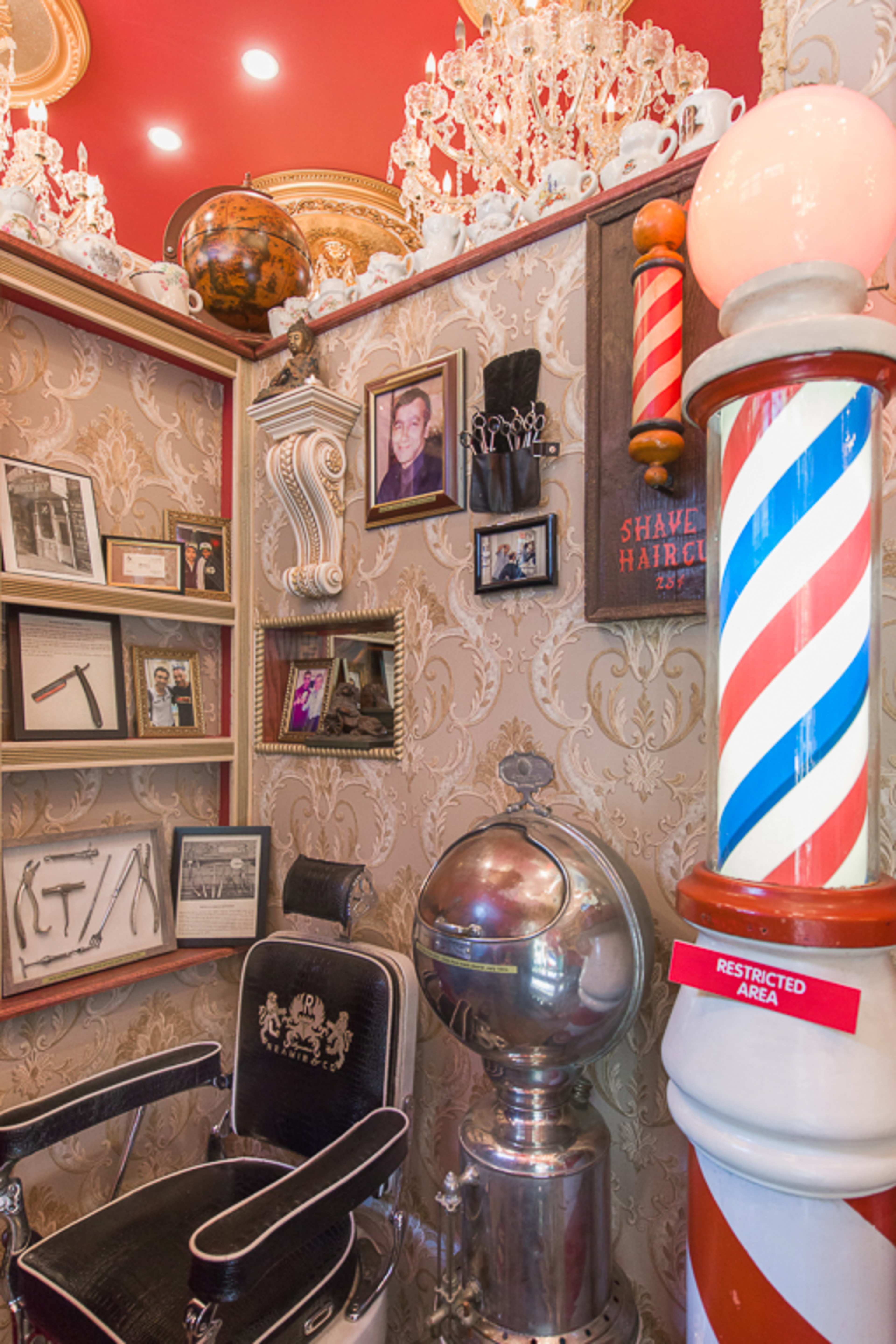 A corner of a vintage barbershop, featuring a barber chair, antique decor, framed photos, and a classic barber pole.