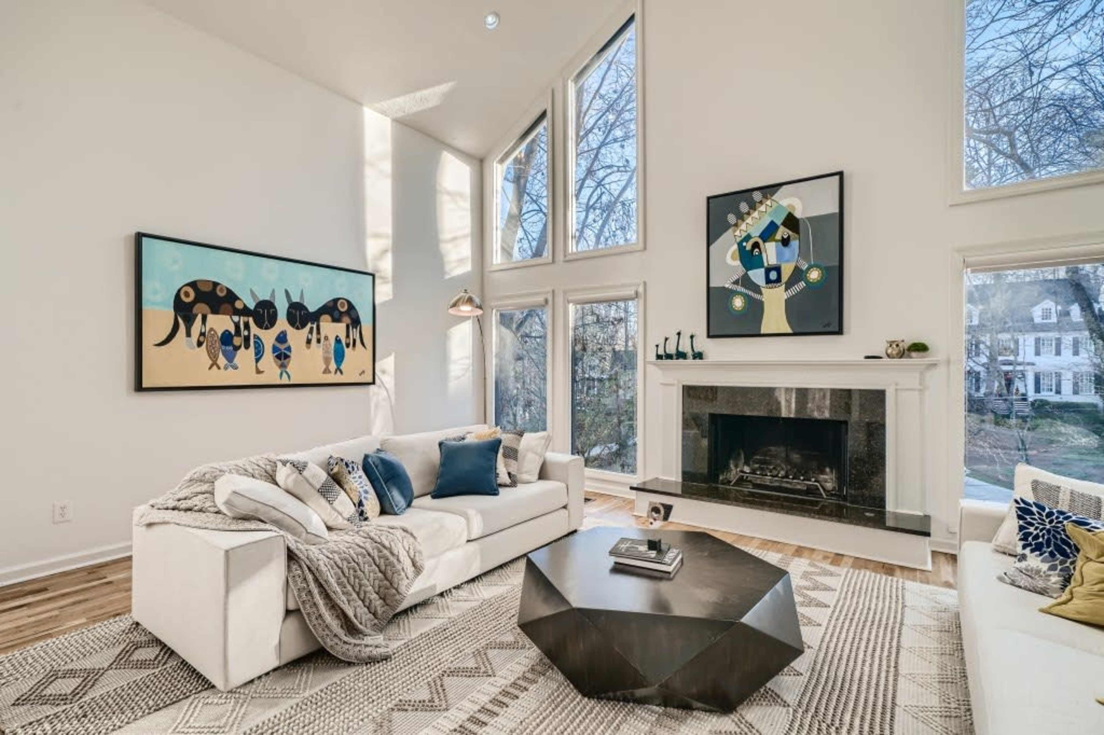 A bright living room features large windows, a modern fireplace, and contemporary artwork on the walls.