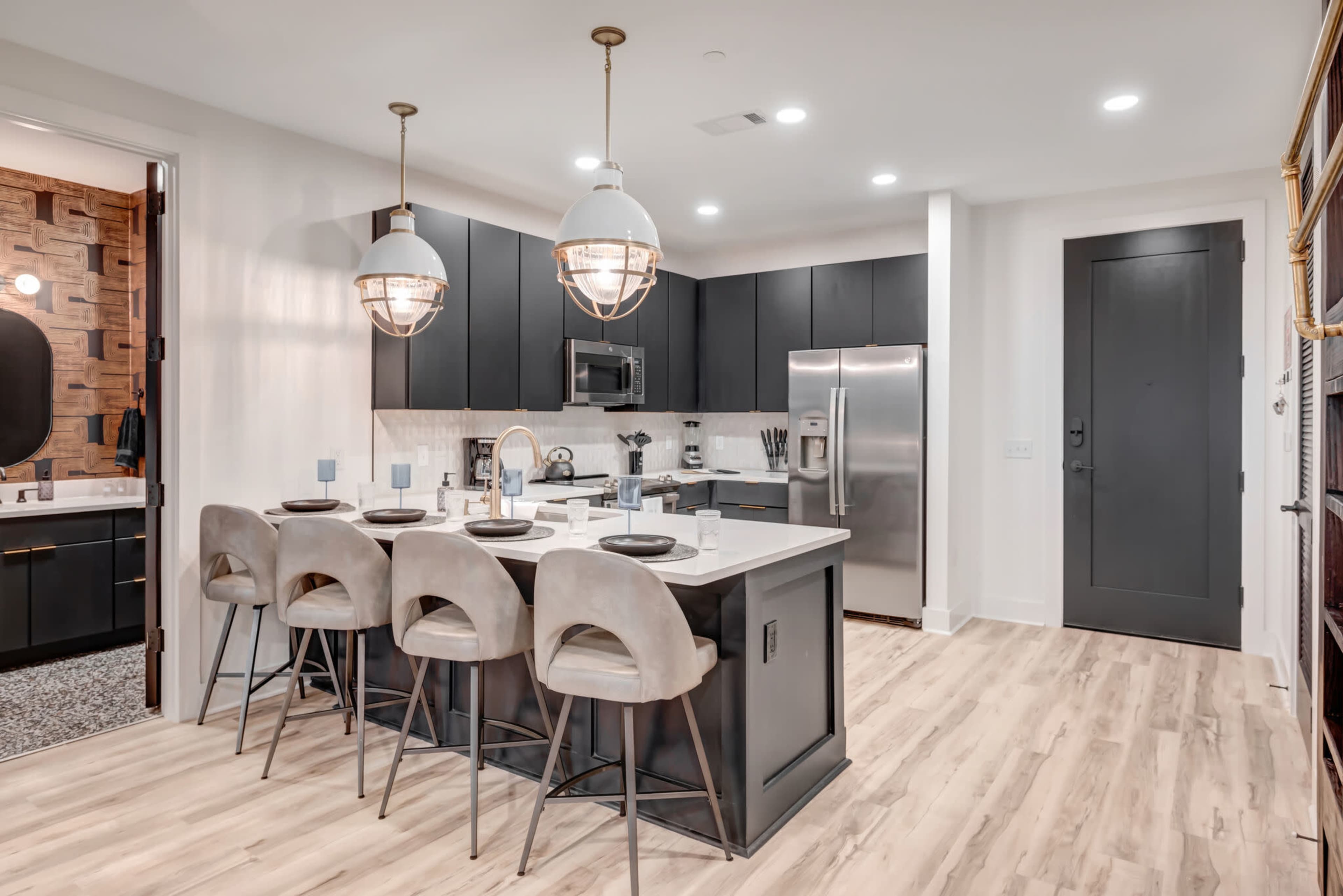 A modern kitchen with dark cabinetry, a large island with seating, and stainless steel appliances.
