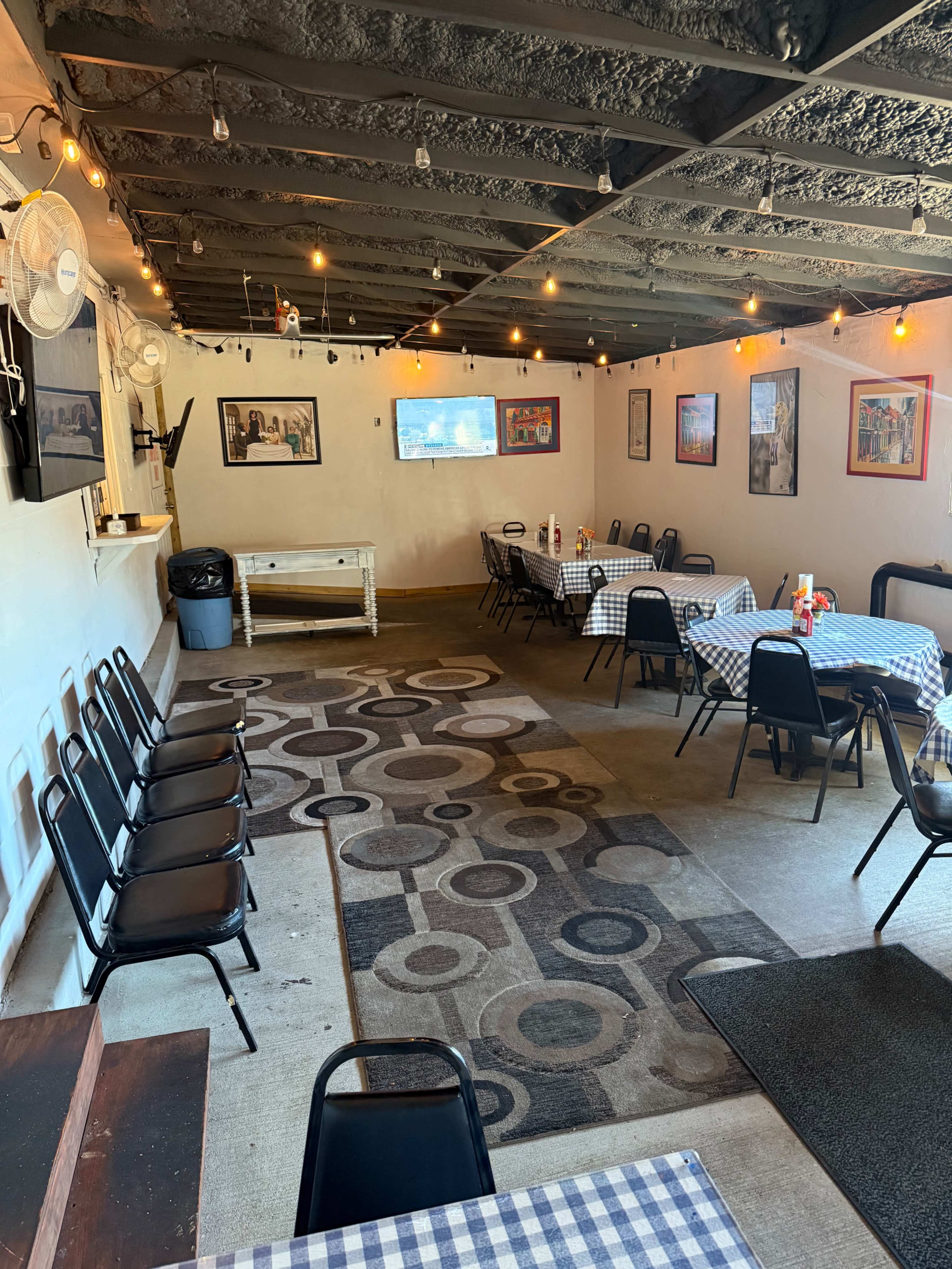 The image shows a dining area in a restaurant featuring several tables with blue and white checkered tablecloths, black chairs, and wall decorations.