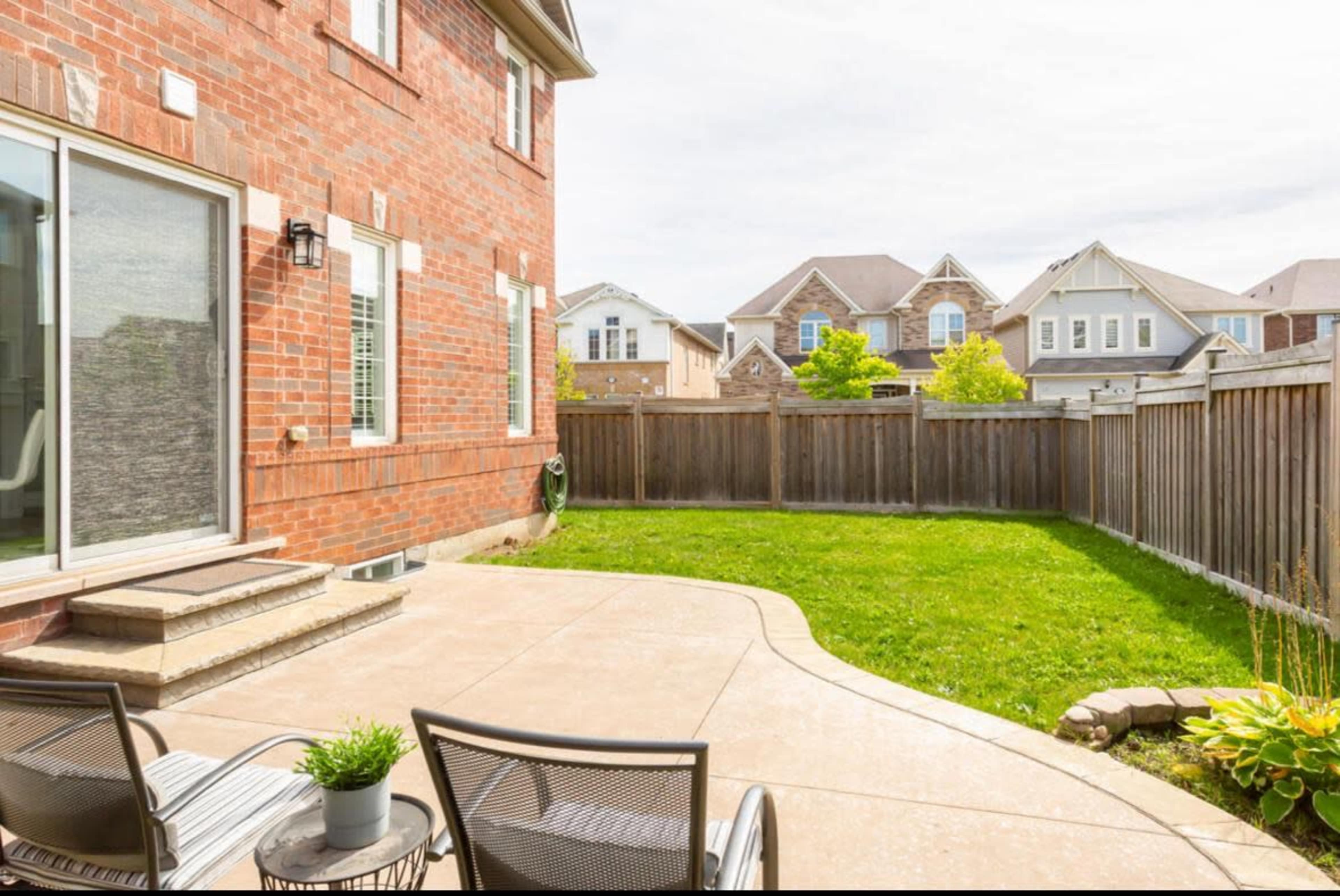 A spacious backyard features a patio with two chairs, surrounded by a grassy area and bordered by wooden fencing.