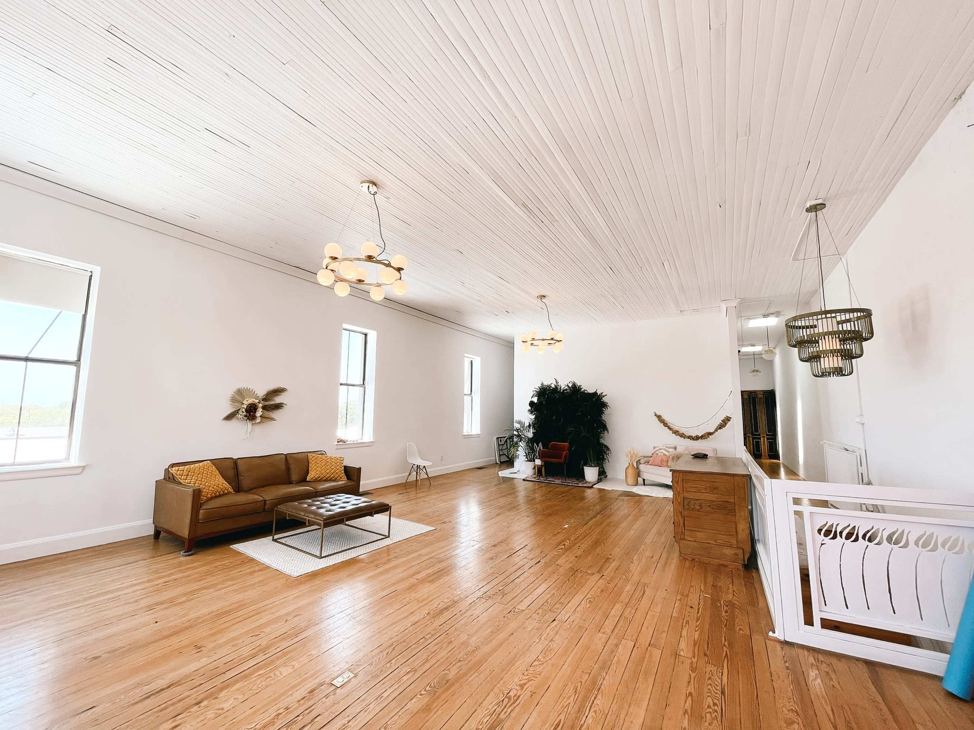 A spacious, well-lit interior with wooden flooring, a brown sofa, modern light fixtures, and large windows.